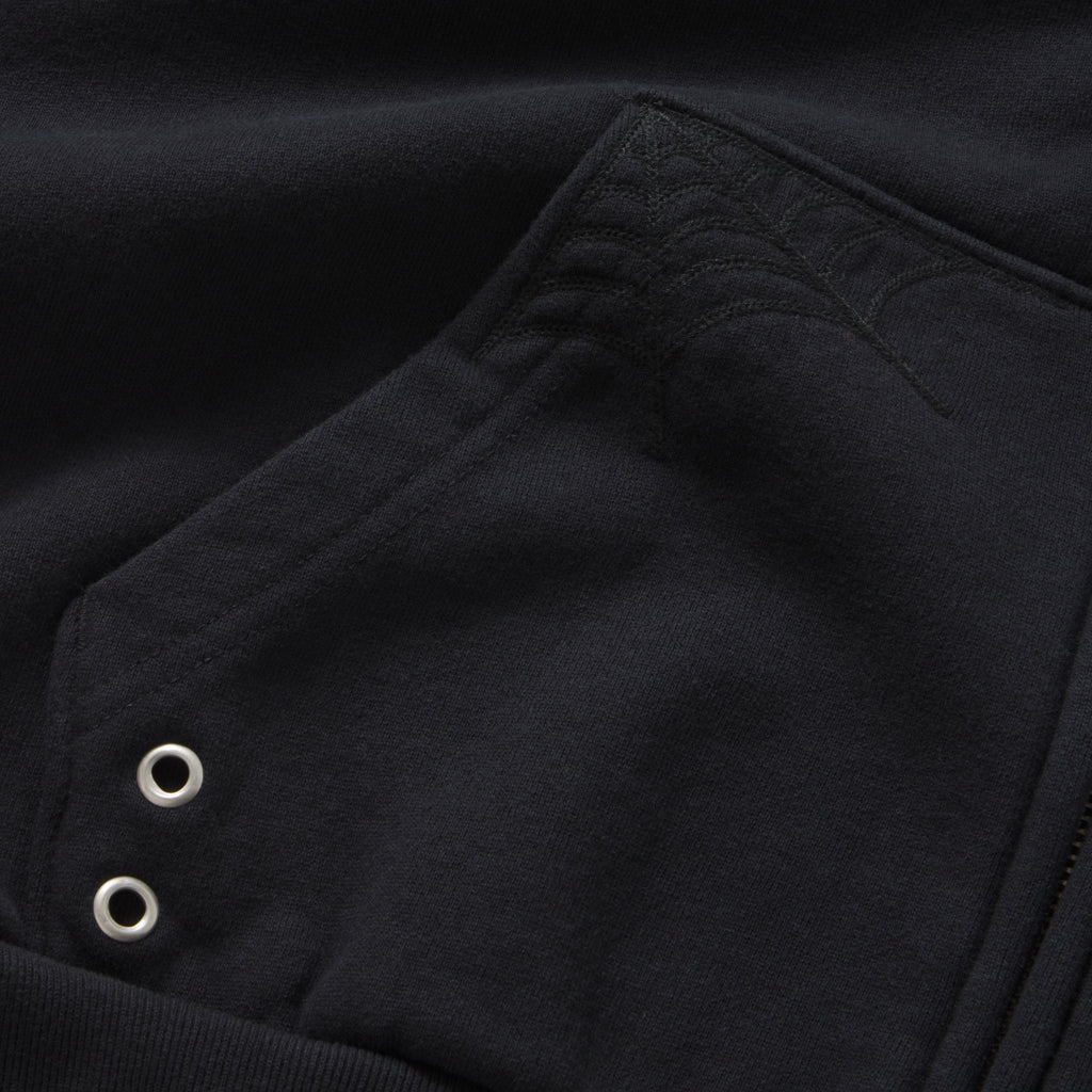 Black 13oz cotton fleece zip hoodie featuring tonal web embroidery on the pocket and silver metal grommet detailing.