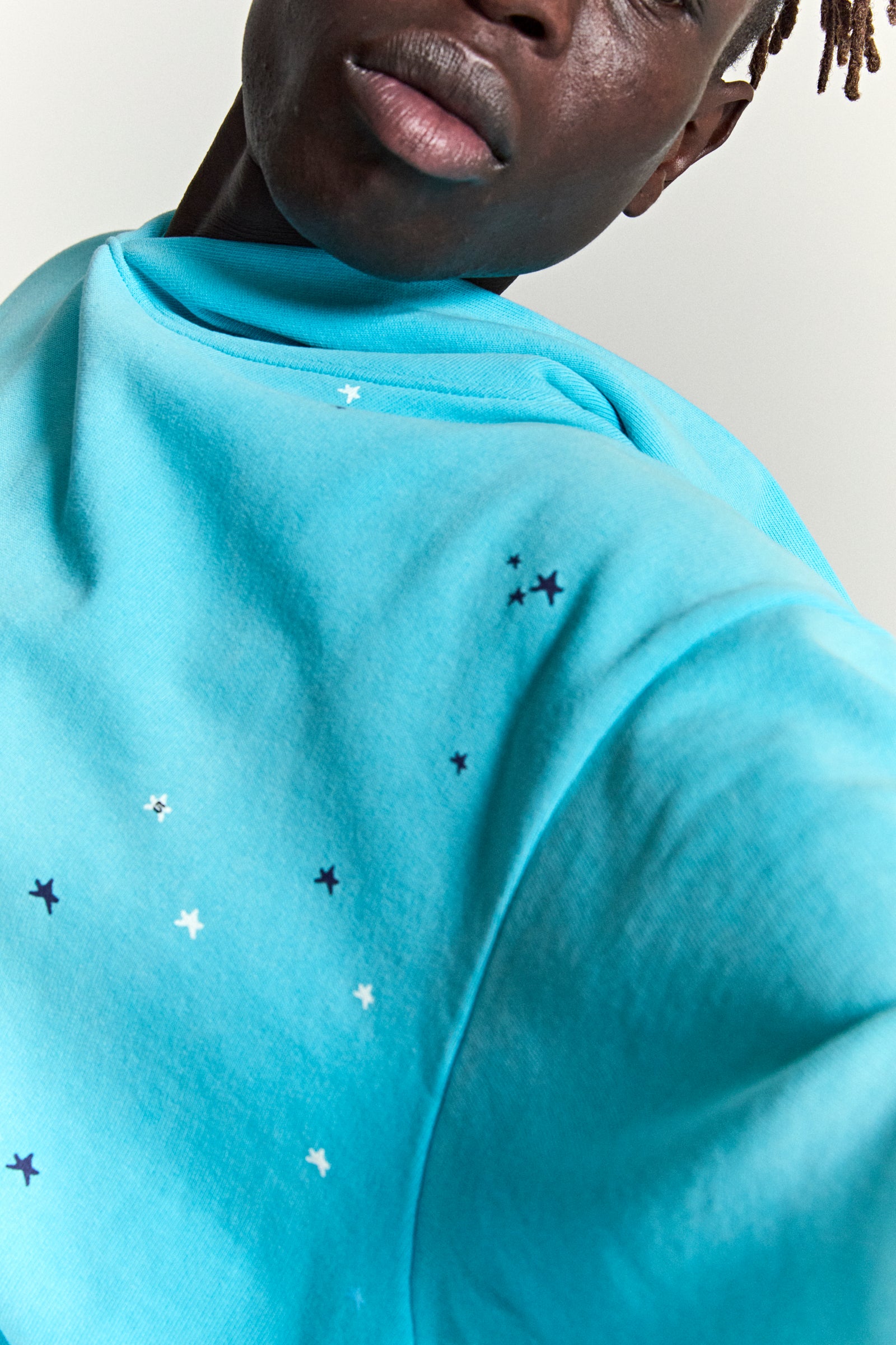 Turquoise heavy web hoodie with scattered white and black star prints on the shoulder.