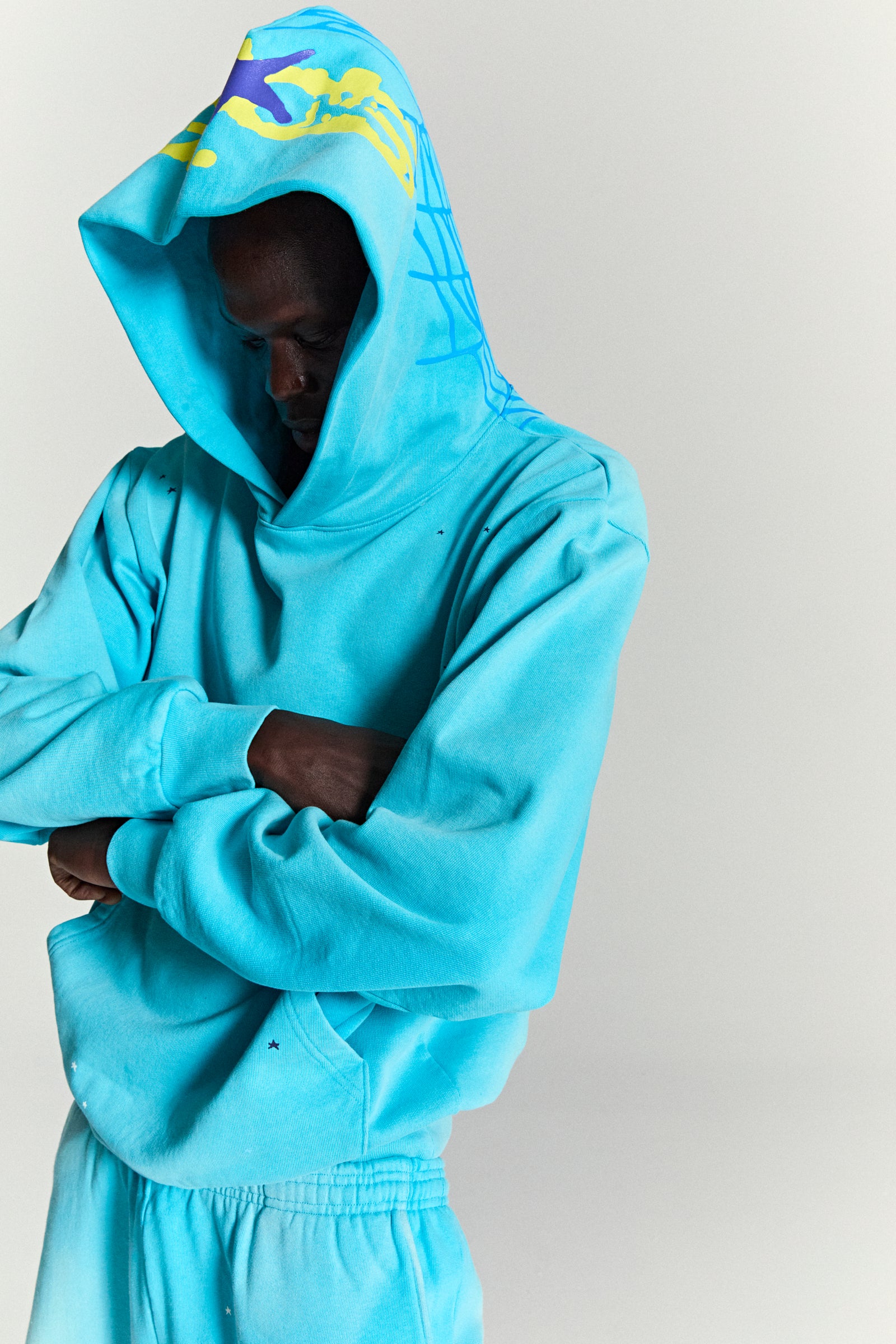 Turquoise HEAVY WEB HOODIE with yellow and purple puff print stars, blue web print on hood.