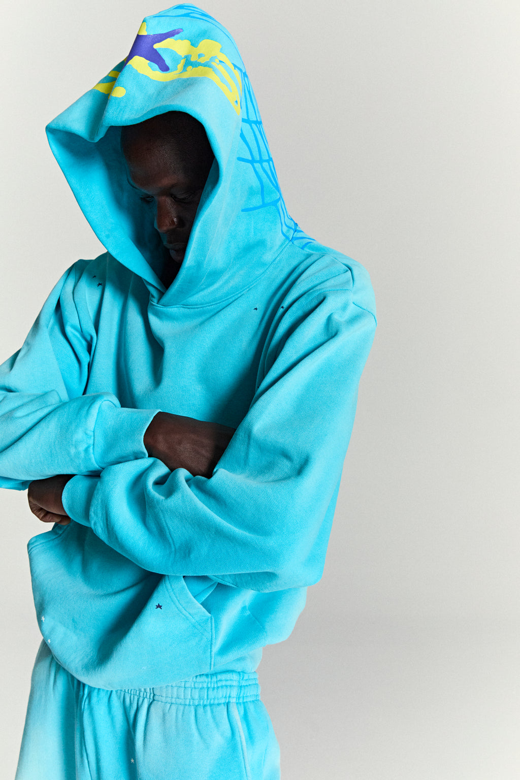 Turquoise HEAVY WEB HOODIE with yellow and purple puff print stars, blue web print on hood.