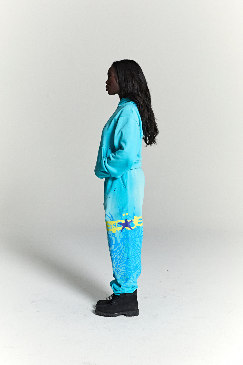 Woman in a turquoise heavy web hoodie and matching sweatpants with star and web prints.