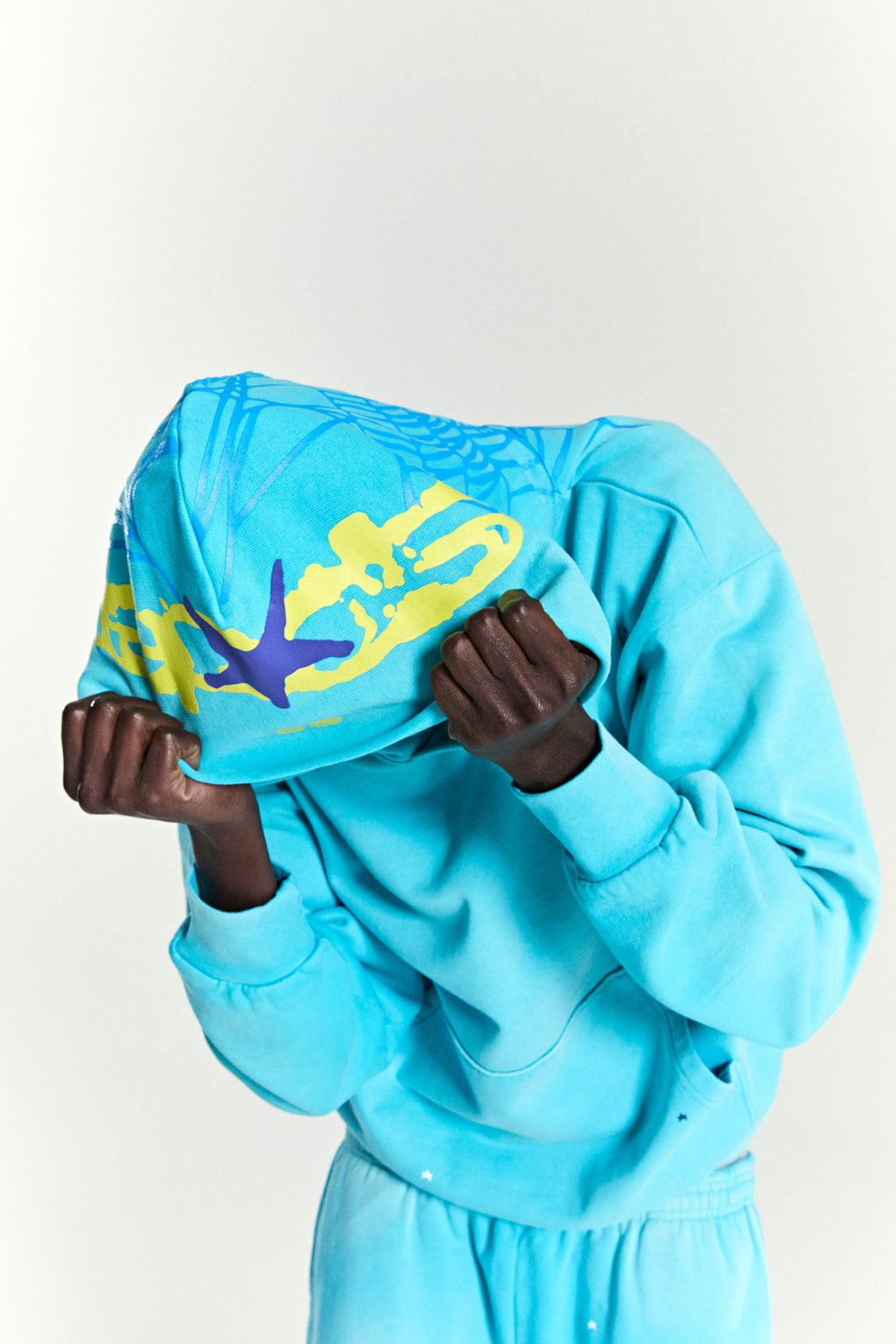 Turquoise heavy web hoodie with yellow and purple star and web puff print designs.