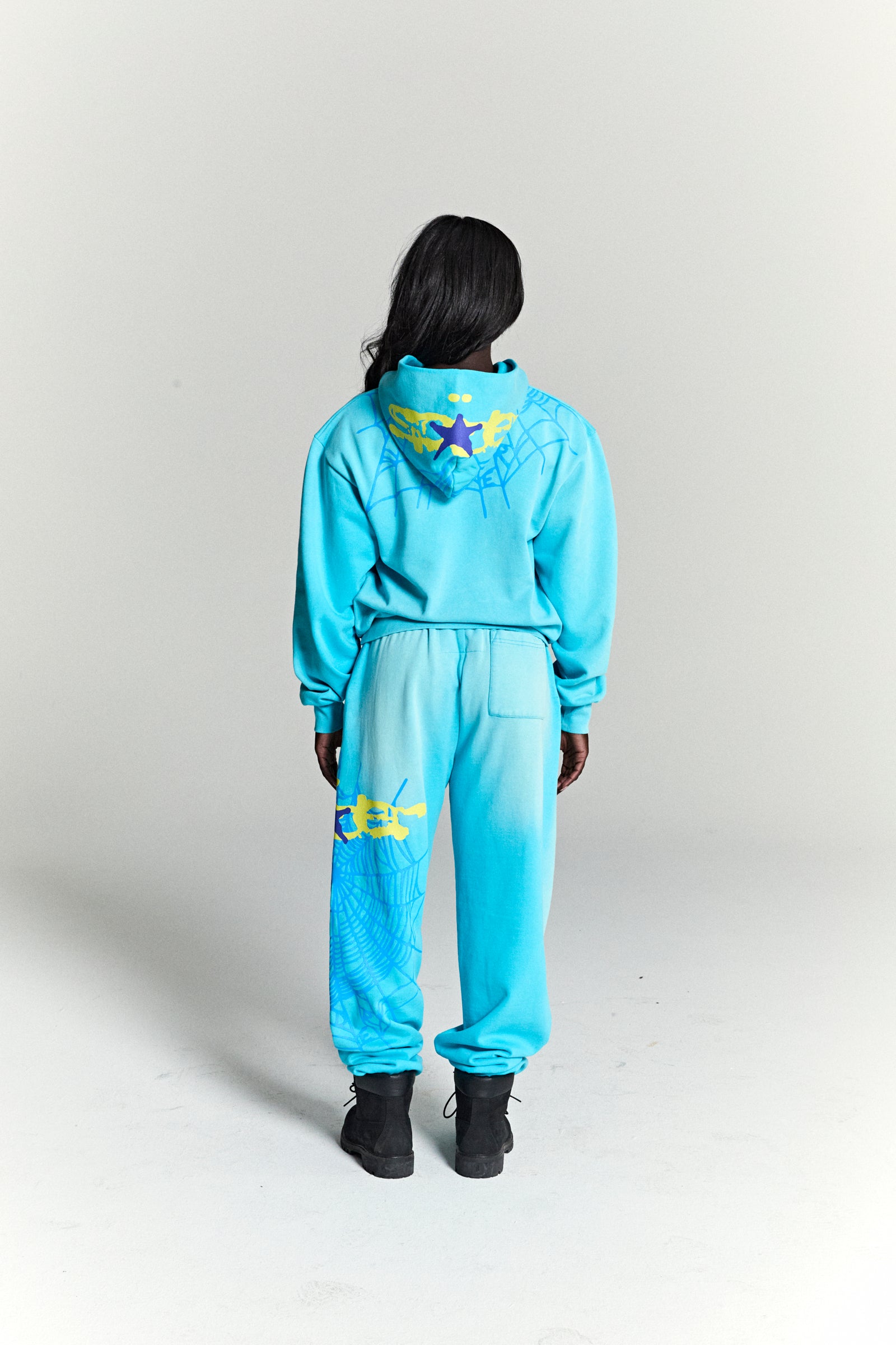 Model from behind wearing a blue HEAVY WEB HOODIE and matching sweatpants with web and star prints.