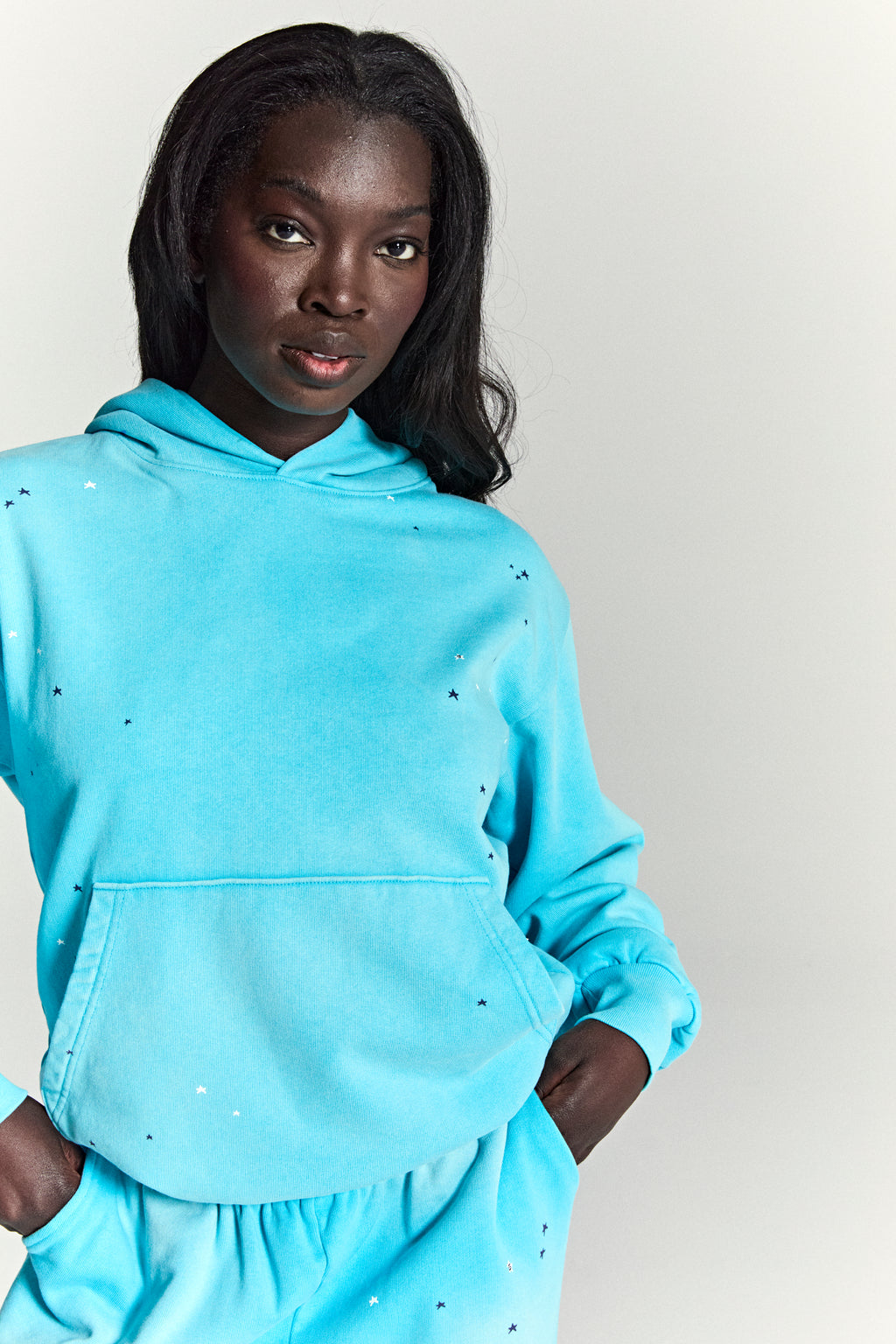 Model in a turquoise heavy web hoodie with scattered star print, kangaroo pocket, and matching sweatpants.