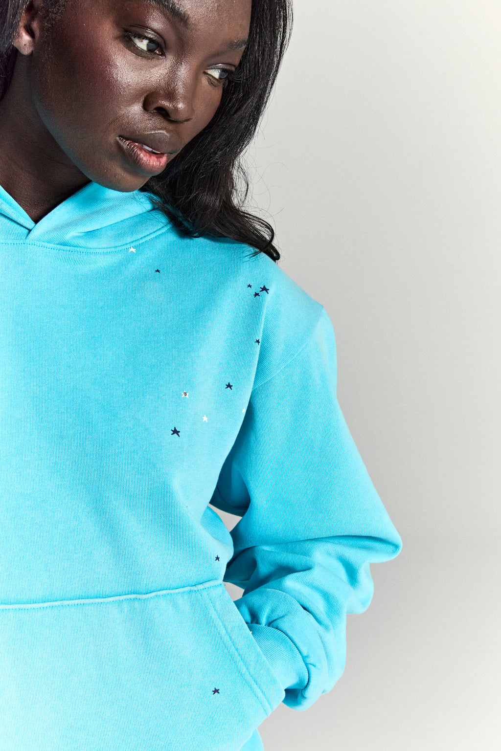 Black model in a turquoise HEAVY WEB HOODIE with scattered star print and kangaroo pocket.