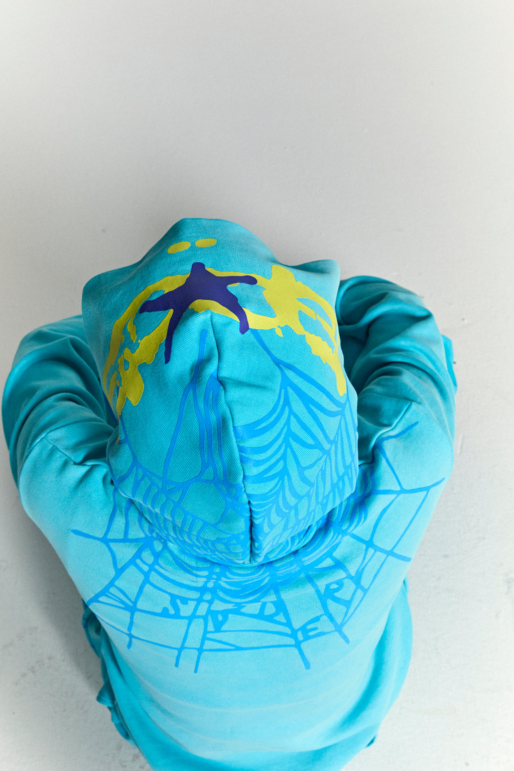 Aqua blue heavy web hoodie with yellow and purple star print on hood, and light blue spider web print on back.