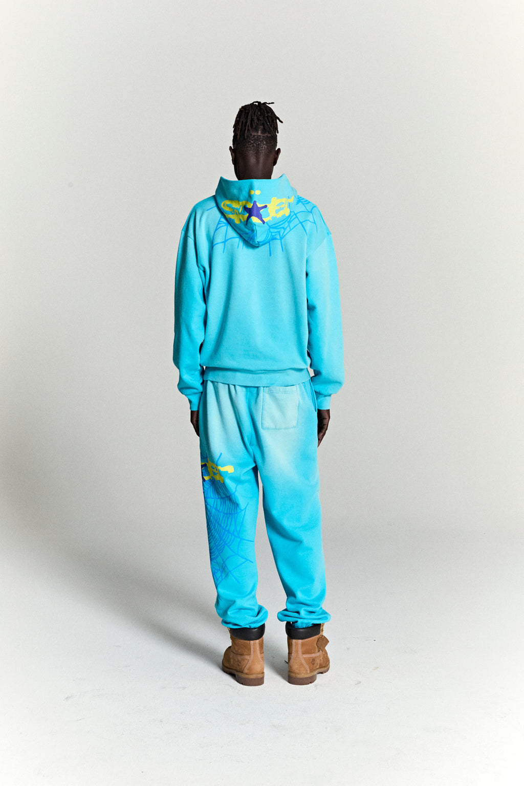 Man from behind wearing a blue heavy web hoodie and matching sweatpants with yellow star and web prints.
