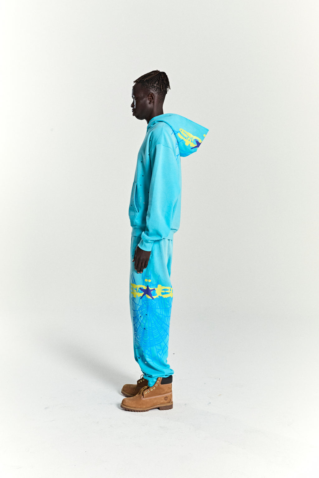 Model in turquoise HEAVY WEB HOODIE and matching sweatpants with yellow puff print stars and web design.