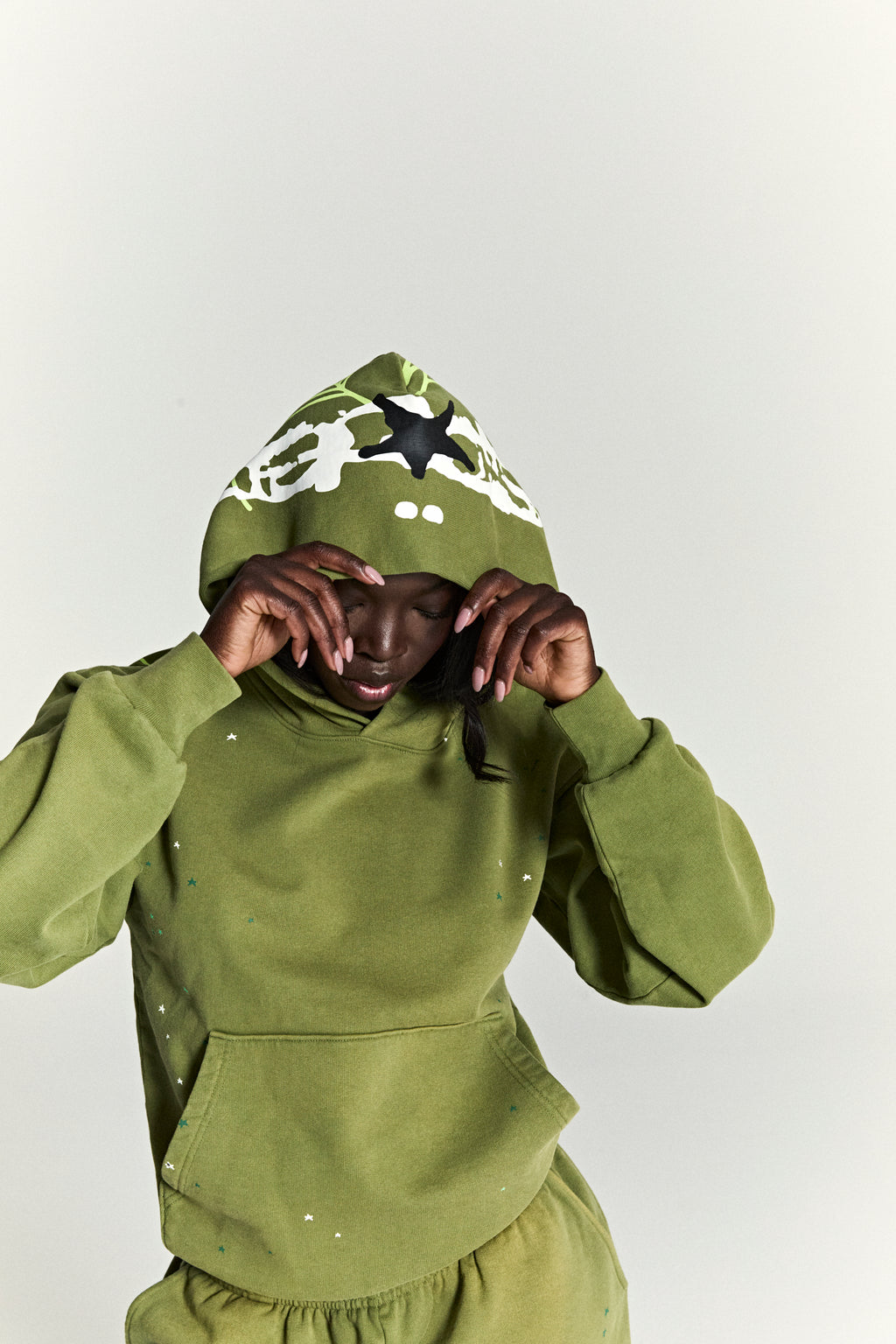 Olive green 13oz cotton fleece hoodie with scattered star print and web print on hood.