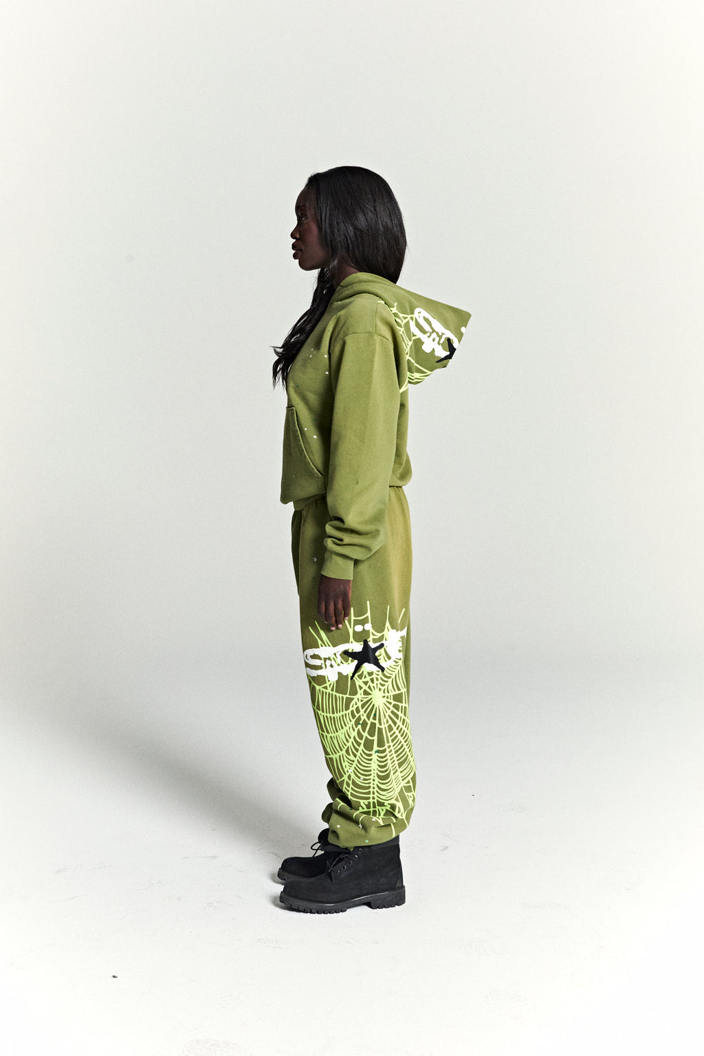 Woman in a green HEAVY WEB HOODIE and matching sweatpants with white web and star prints.