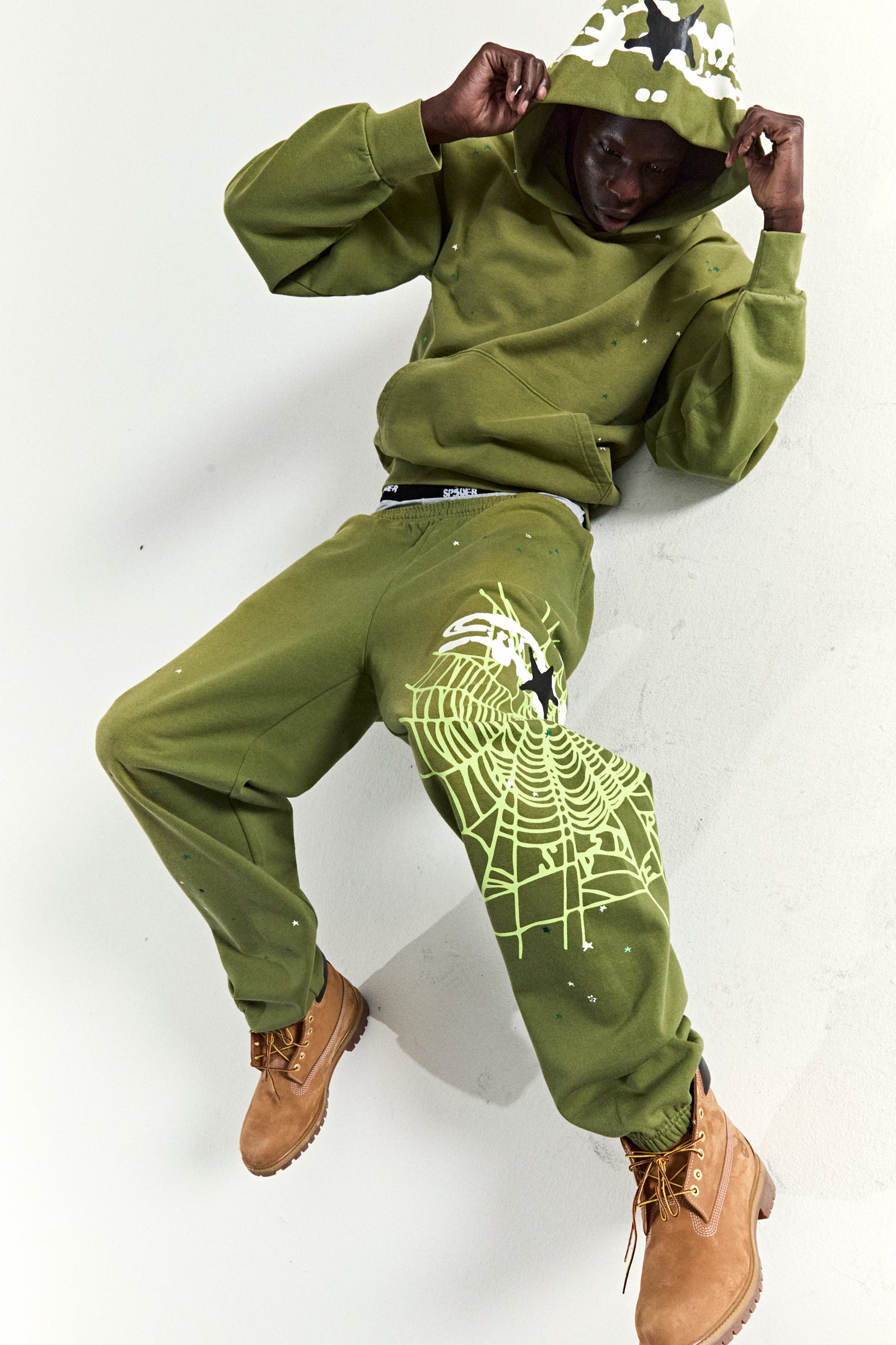 Olive green heavy web hoodie and sweatpants with star and web puff prints, worn by a model.