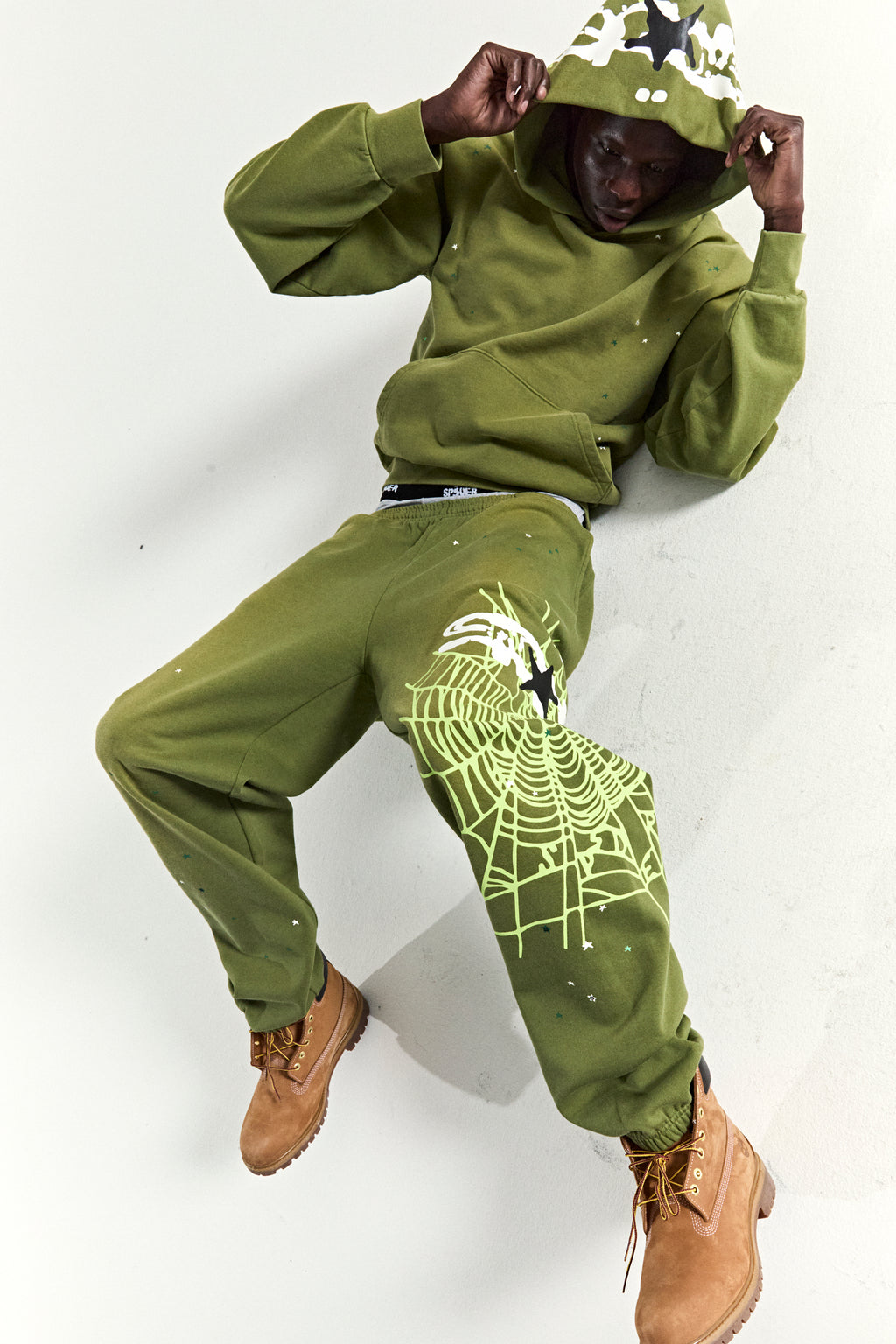 Olive green heavy web hoodie and sweatpants with star and web puff prints, worn by a model.