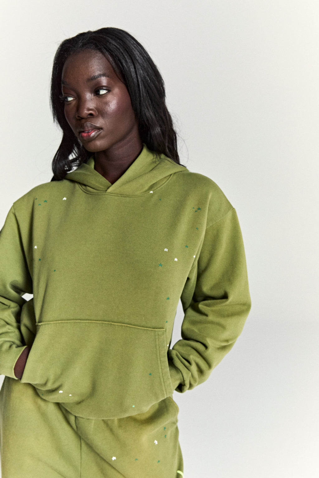 Woman in an olive green cotton fleece hoodie with scattered star print and a kangaroo pocket.