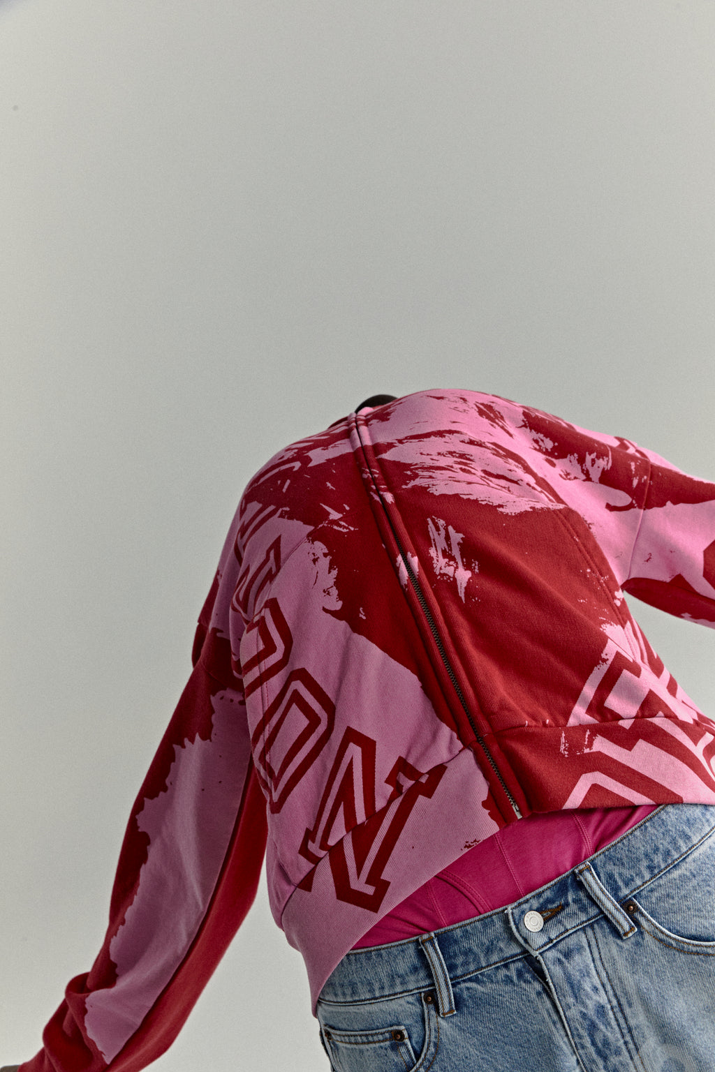 Red and pink color-blocked cotton fleece zip hoodie with varsity lettering and blue jeans.