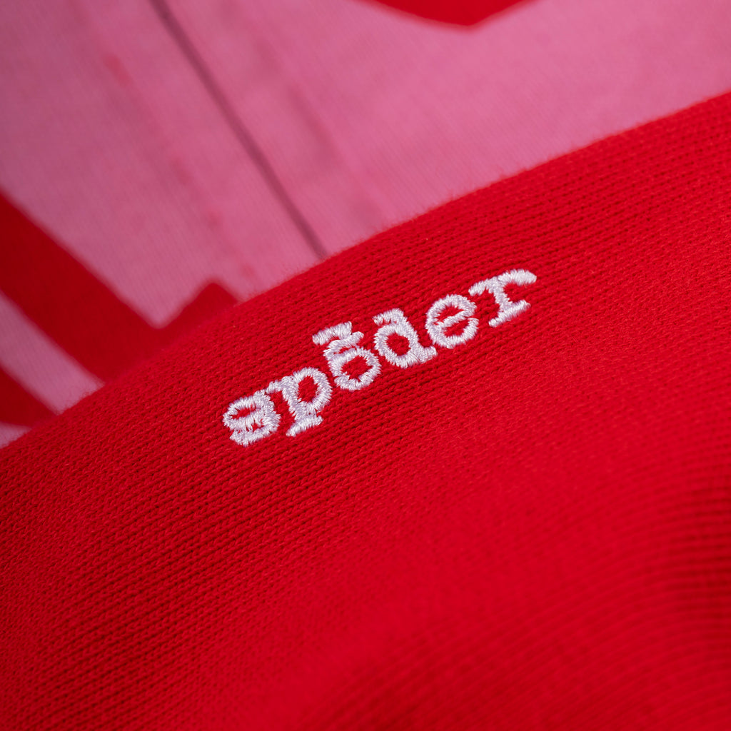 Close-up of a red cotton fleece hoodie with white embroidered "spēder" logo on the sleeve.