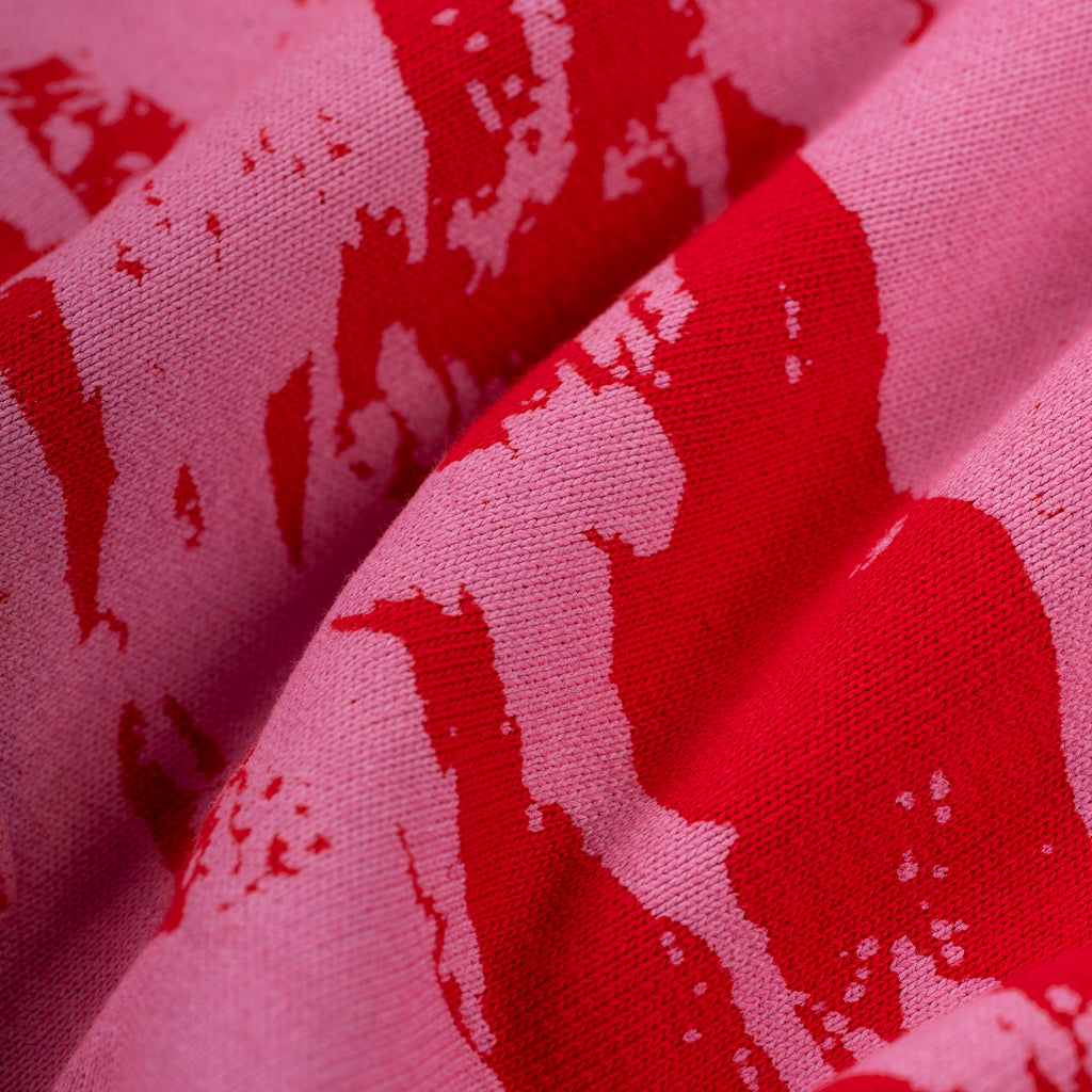 Close-up of pink 100% cotton fleece with a bold red color-blocked, distressed varsity-style pattern.