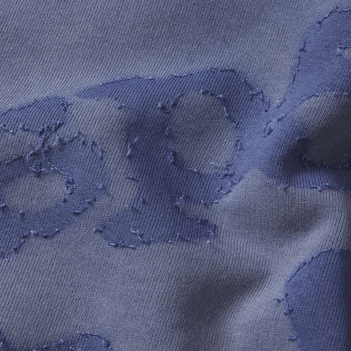 Close-up of blue 100% cotton fleece hoodie featuring a distressed SP5DER graphic print with textured applique details.