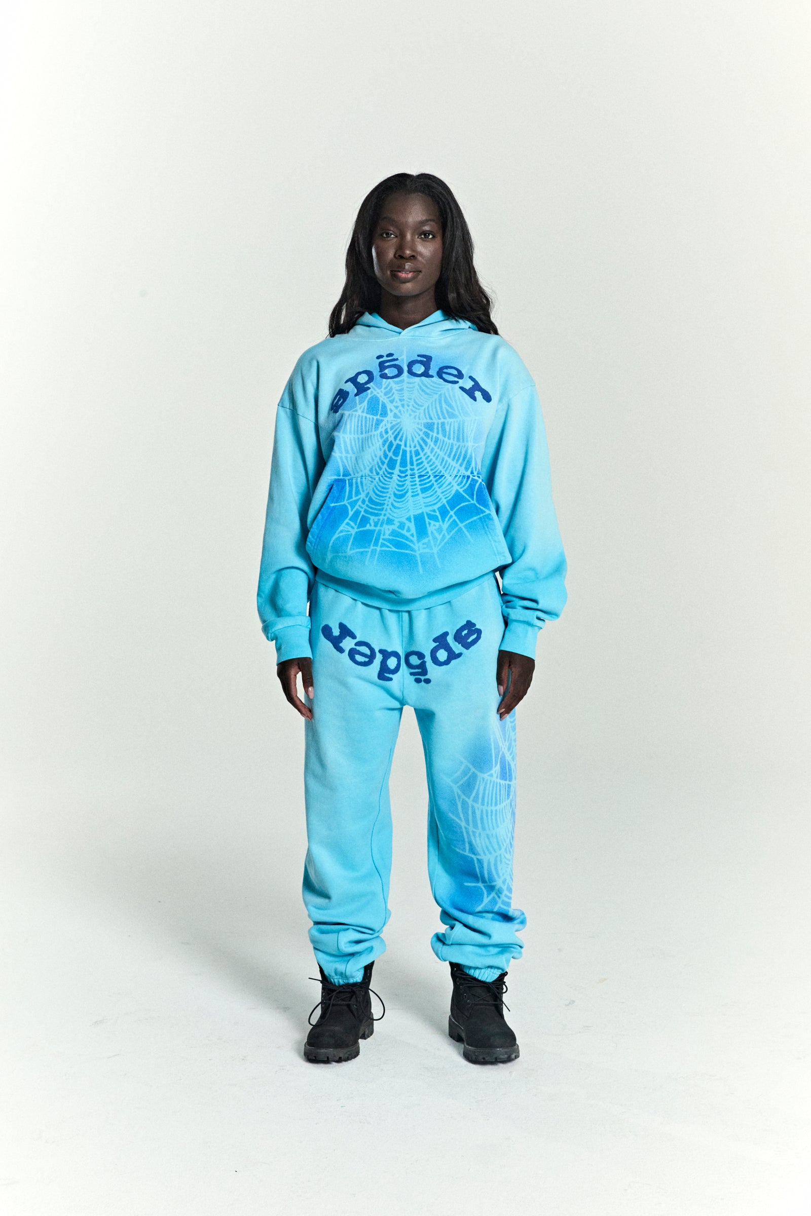 Woman in light blue OG WEB V2 SPRAY HOODIE and matching sweatpants with spiderweb and "spider" print.