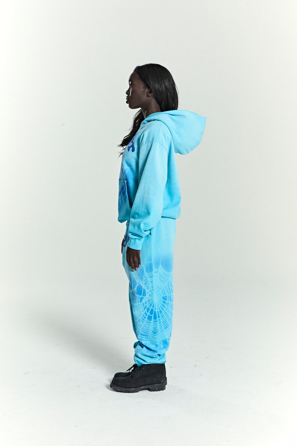 Model in light blue OG WEB V2 SPRAY HOODIE and matching sweatpants with spiderweb print.