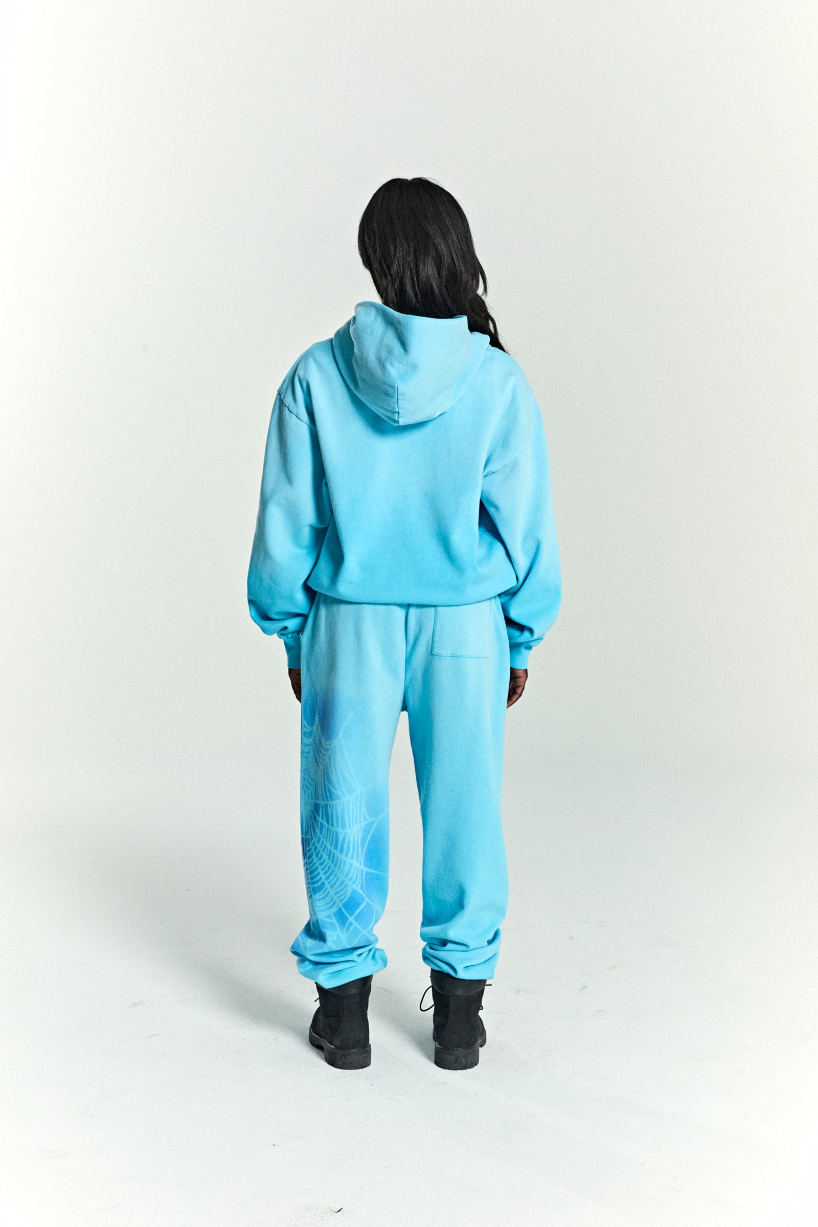 Person from behind wearing a light blue OG WEB V2 SPRAY HOODIE and matching sweatpants with a white spiderweb print.