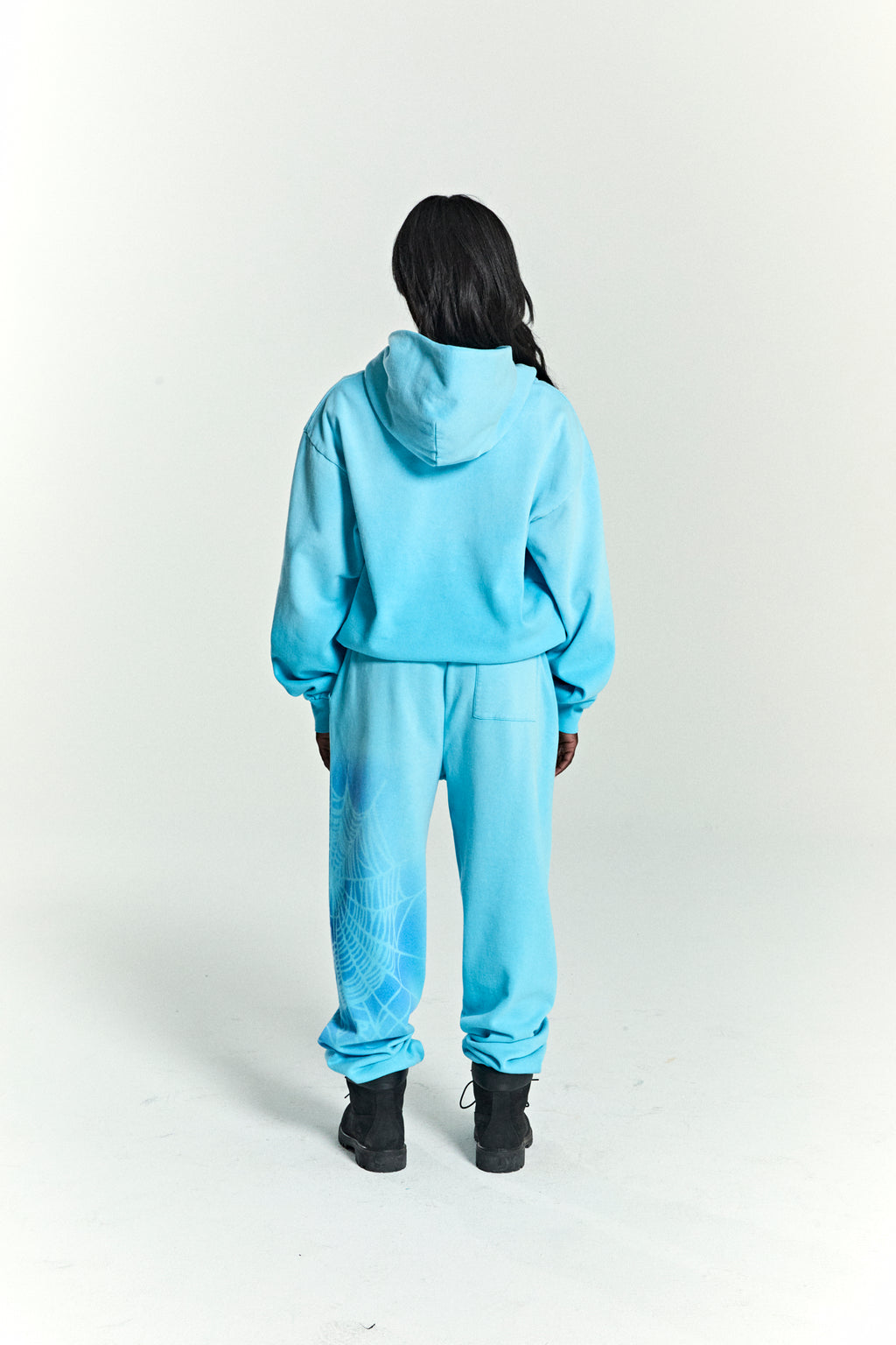 Person from behind wearing a light blue OG WEB V2 SPRAY HOODIE and matching sweatpants with a white spiderweb print.
