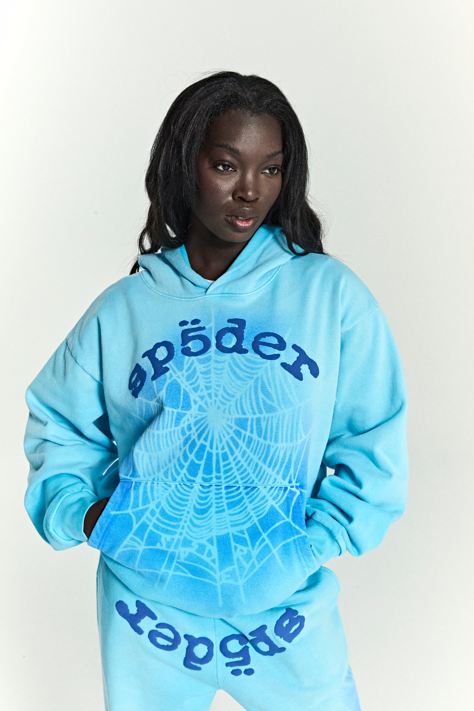 Model wearing light blue OG WEB V2 SPRAY HOODIE with dark blue spiderweb and "sp5der" puff print.