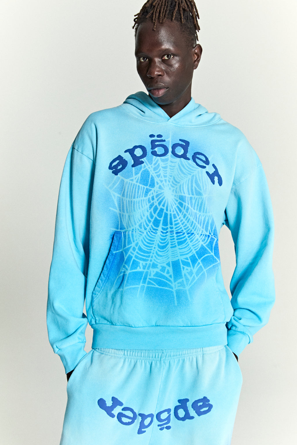 Man in light blue OG WEB V2 SPRAY HOODIE with spiderweb and "Sp5der" puff print.