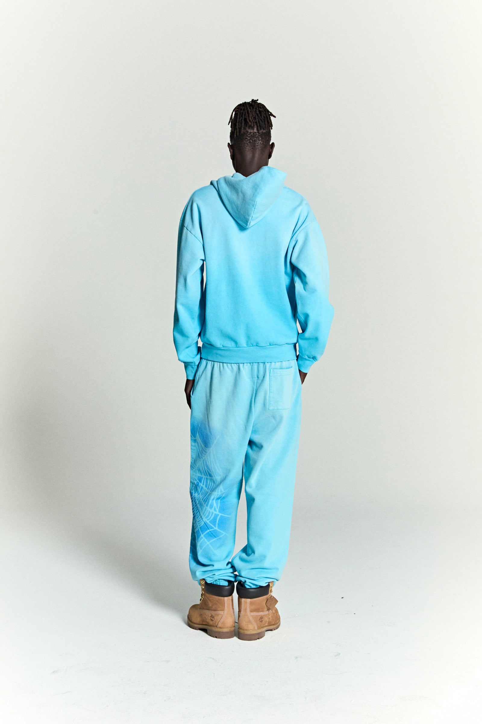 Back view of a light blue cotton fleece hoodie and sweatpants set with a subtle spray web V2 print.