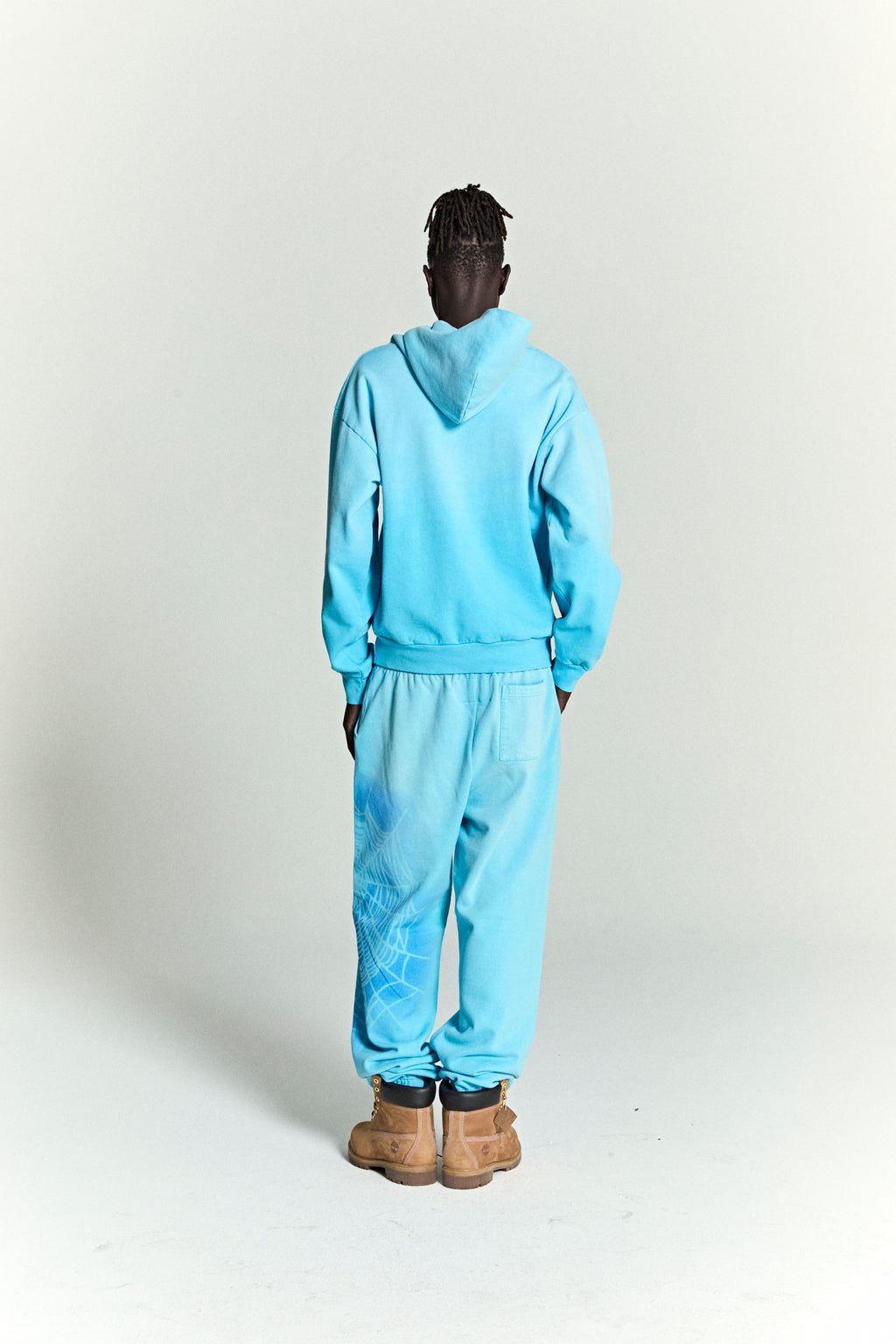 Back view of a light blue cotton fleece hoodie and sweatpants set with a subtle spray web V2 print.