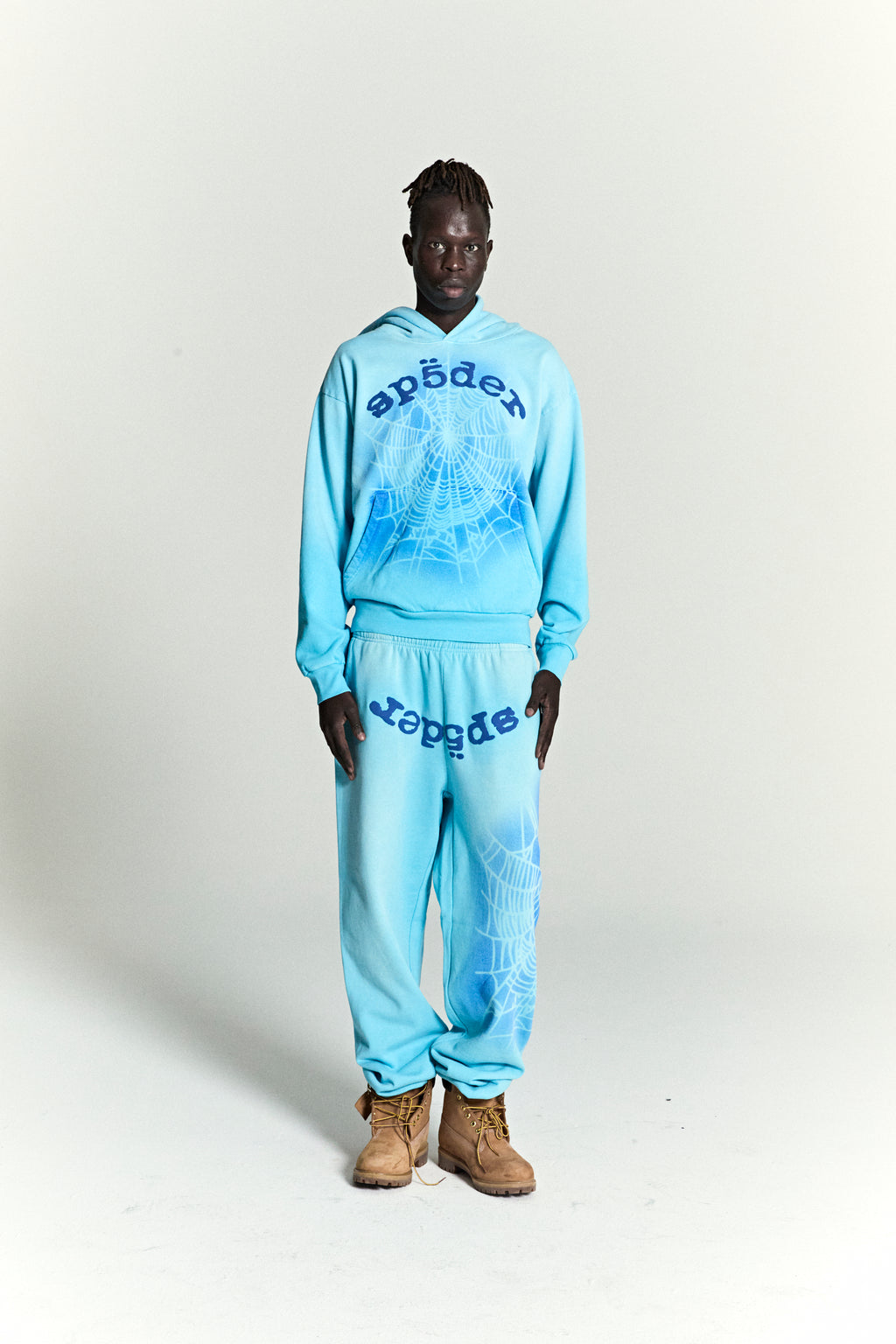 Man in blue OG WEB V2 SPRAY HOODIE and matching sweatpants with spiderweb print.