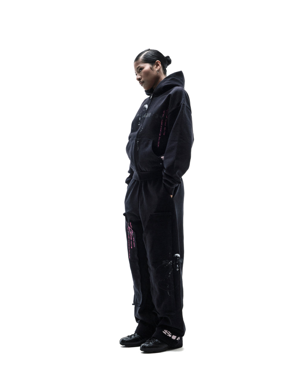 Model wearing a black oversized zip-up hoodie and matching sweatpants with pink graphic accents against a white background.