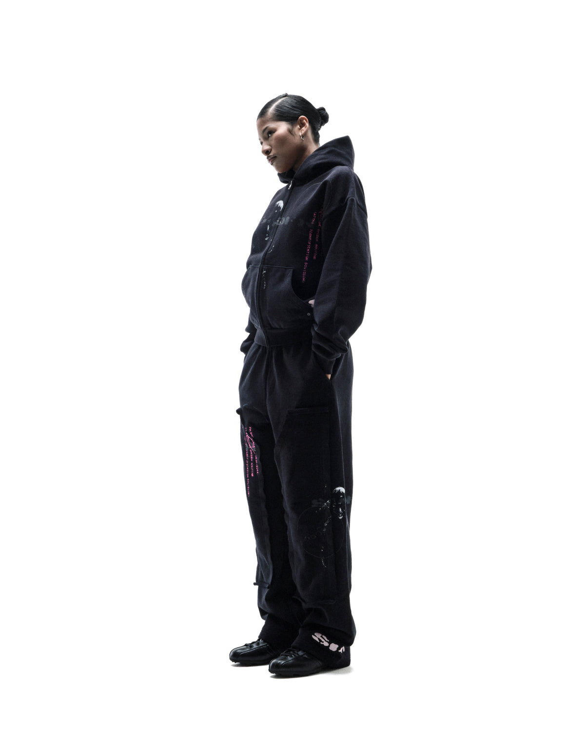 Model wearing a black oversized zip-up hoodie and matching sweatpants with pink graphic accents against a white background.