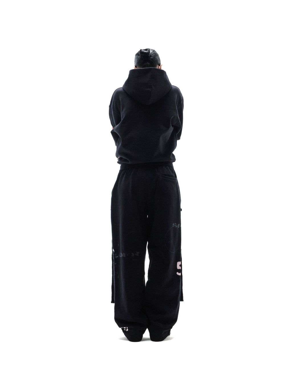 Model standing with back to camera wearing a black oversized hoodie and matching sweatpants with subtle graphic details.
