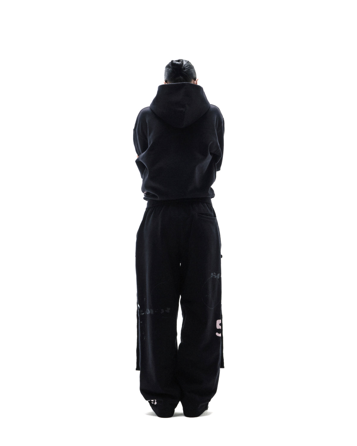 Model standing with back to camera wearing a black oversized hoodie and matching sweatpants with subtle graphic details.