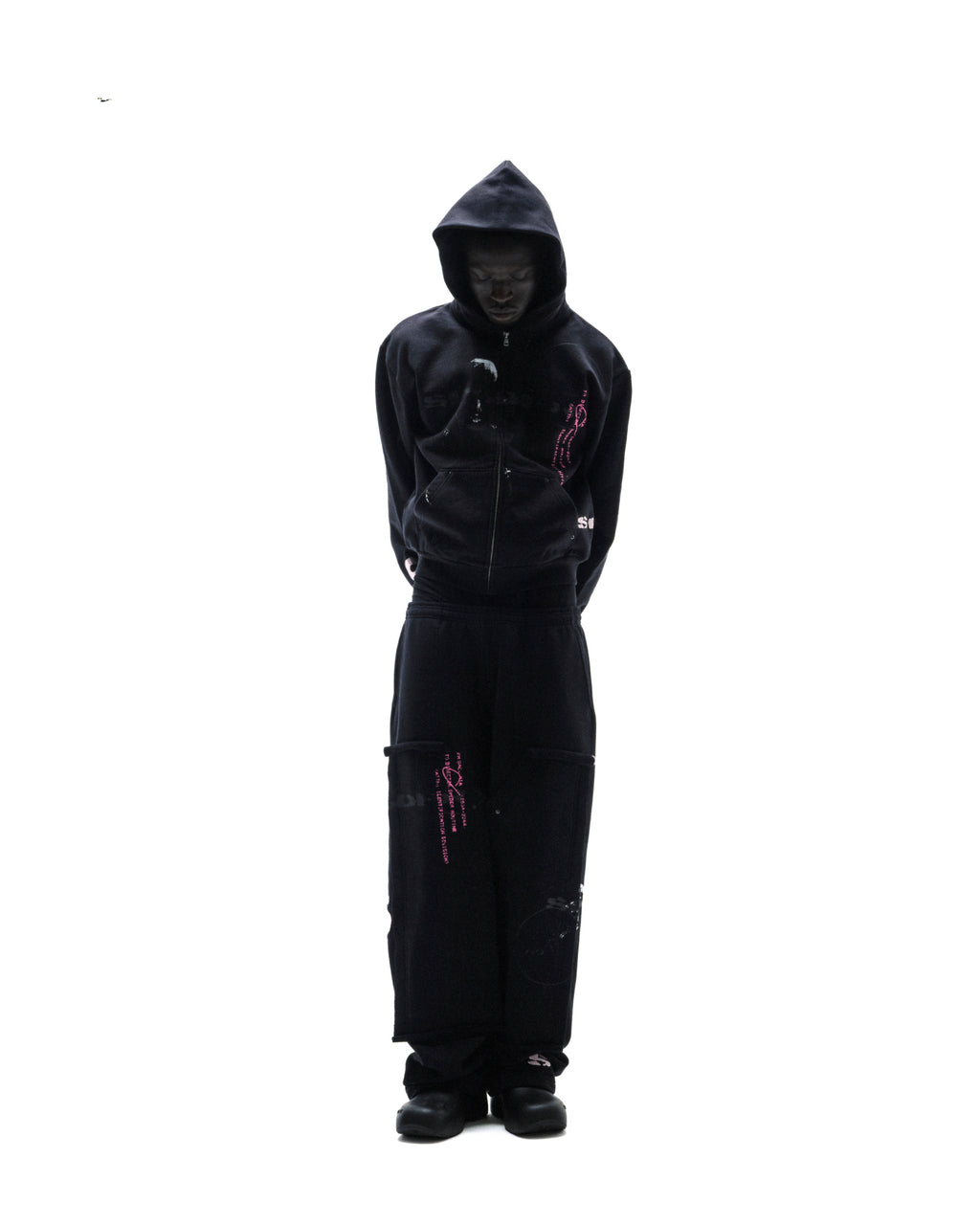 Model wearing a black zip-up hoodie and matching sweatpants with pink graphic prints against a white background.