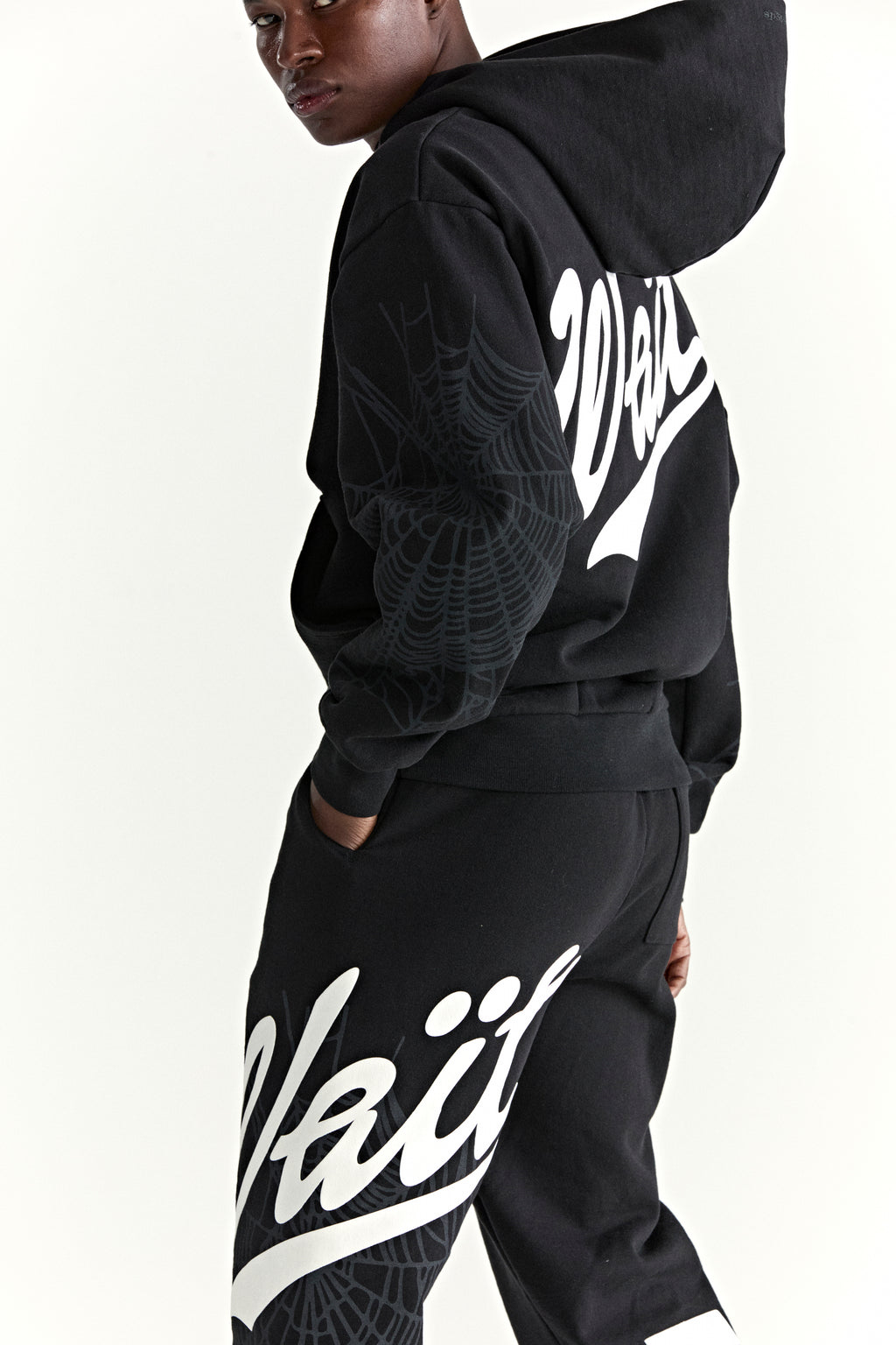 Black 13oz cotton fleece hoodie and sweatpants with "Wait" script, '5' graphic, and spider web detail.