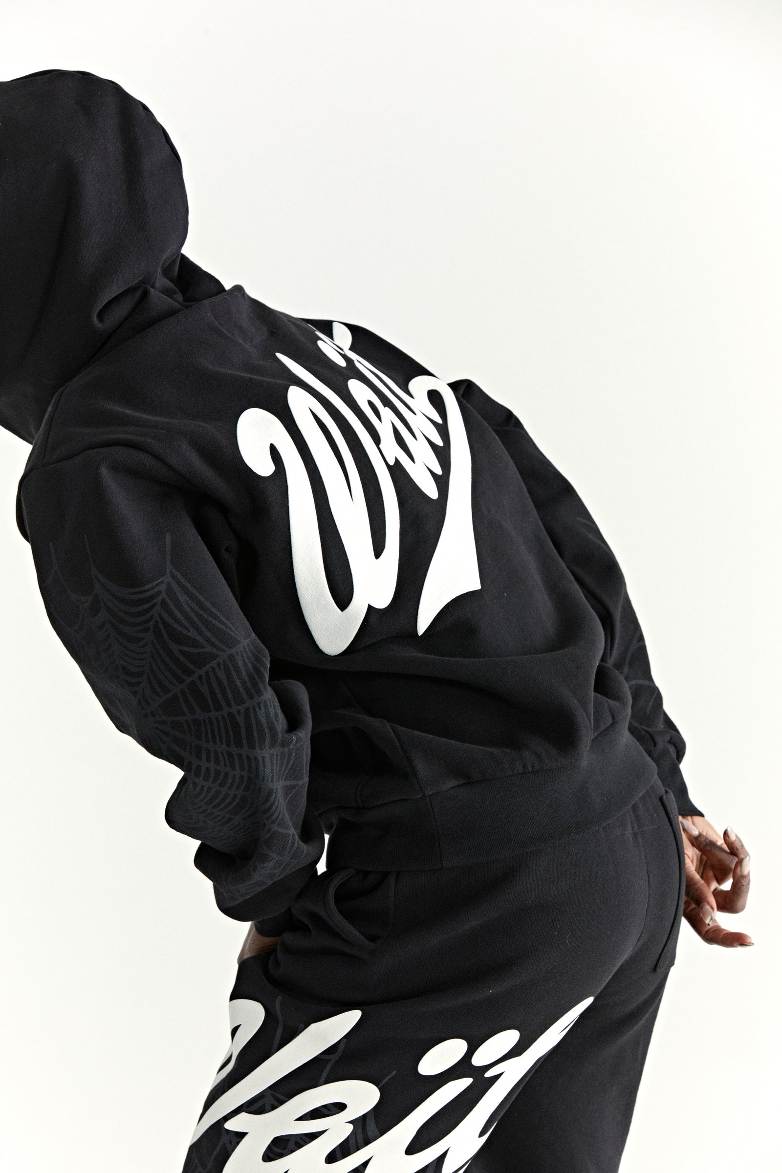 Black 13oz cotton fleece hoodie with "Wait" script on back, spiderweb detail on sleeves.