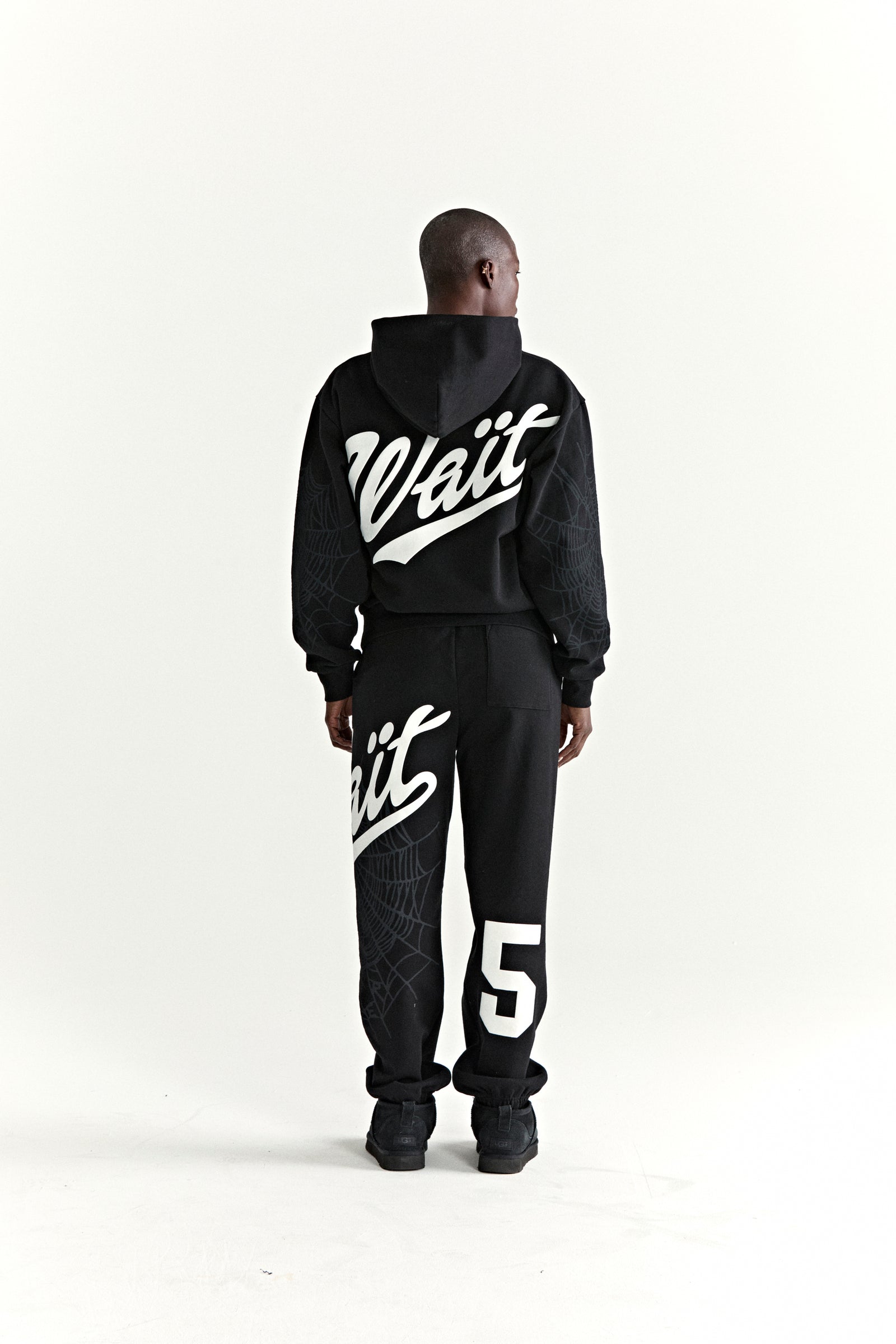 Black 13oz cotton fleece STADIUM HOODIE and sweatpants with white puff print "Wait" text, "5" graphic, and web detail.