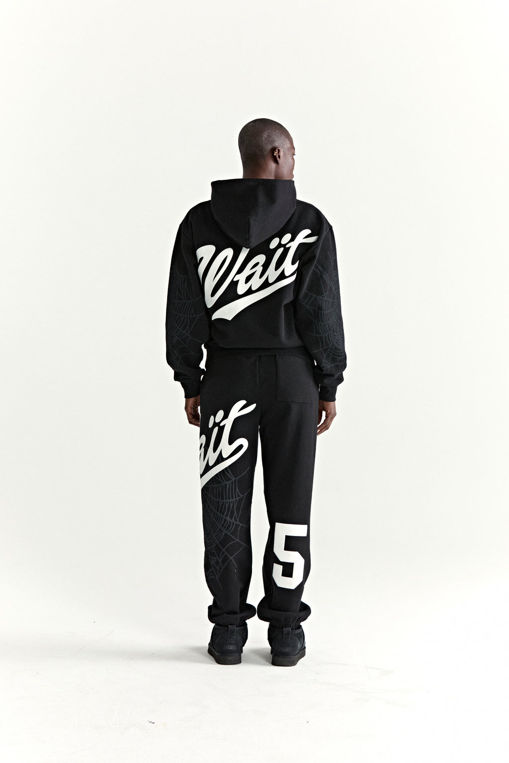 Black 13oz cotton fleece STADIUM HOODIE and sweatpants with white puff print "Wait" text, "5" graphic, and web detail.