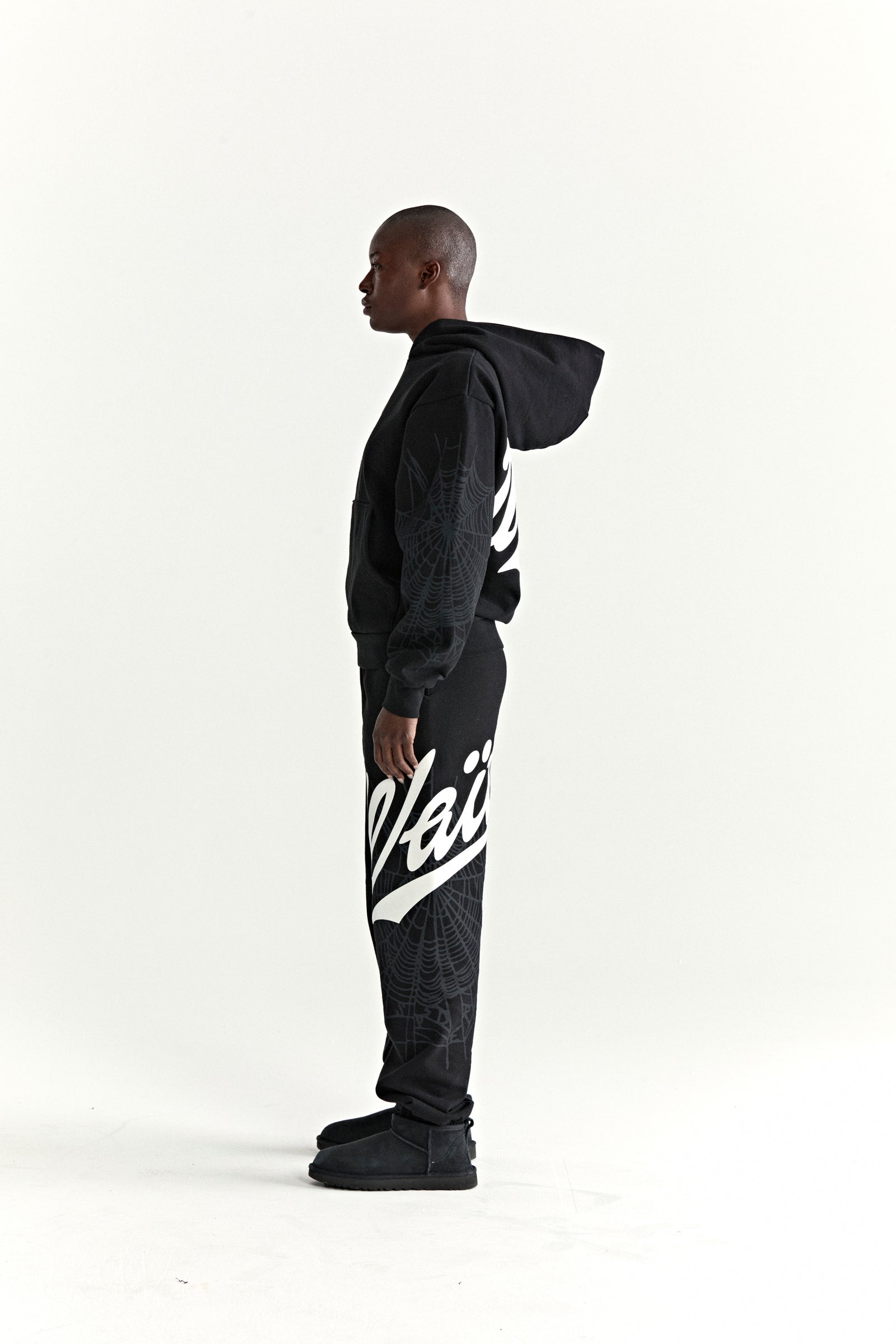 Black 13oz cotton fleece hoodie and sweatpants with white "Wait" script, spiderweb details, and ribbed cuffs.