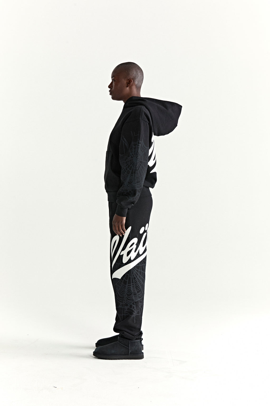 Black 13oz cotton fleece hoodie and sweatpants with white "Wait" script, spiderweb details, and ribbed cuffs.