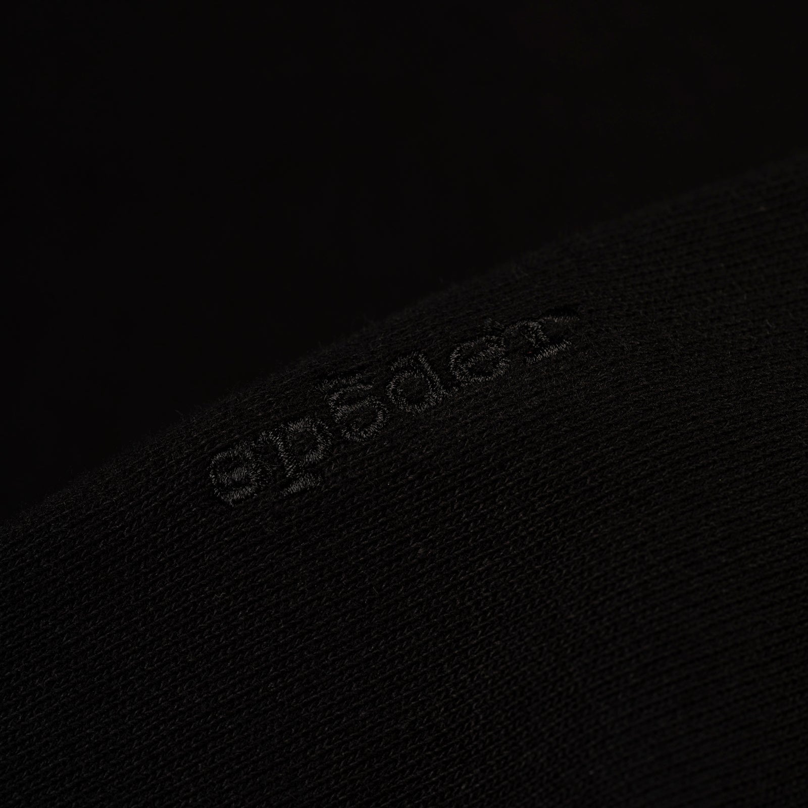 Close-up of a black 100% cotton fleece hoodie with subtle embroidered logo.