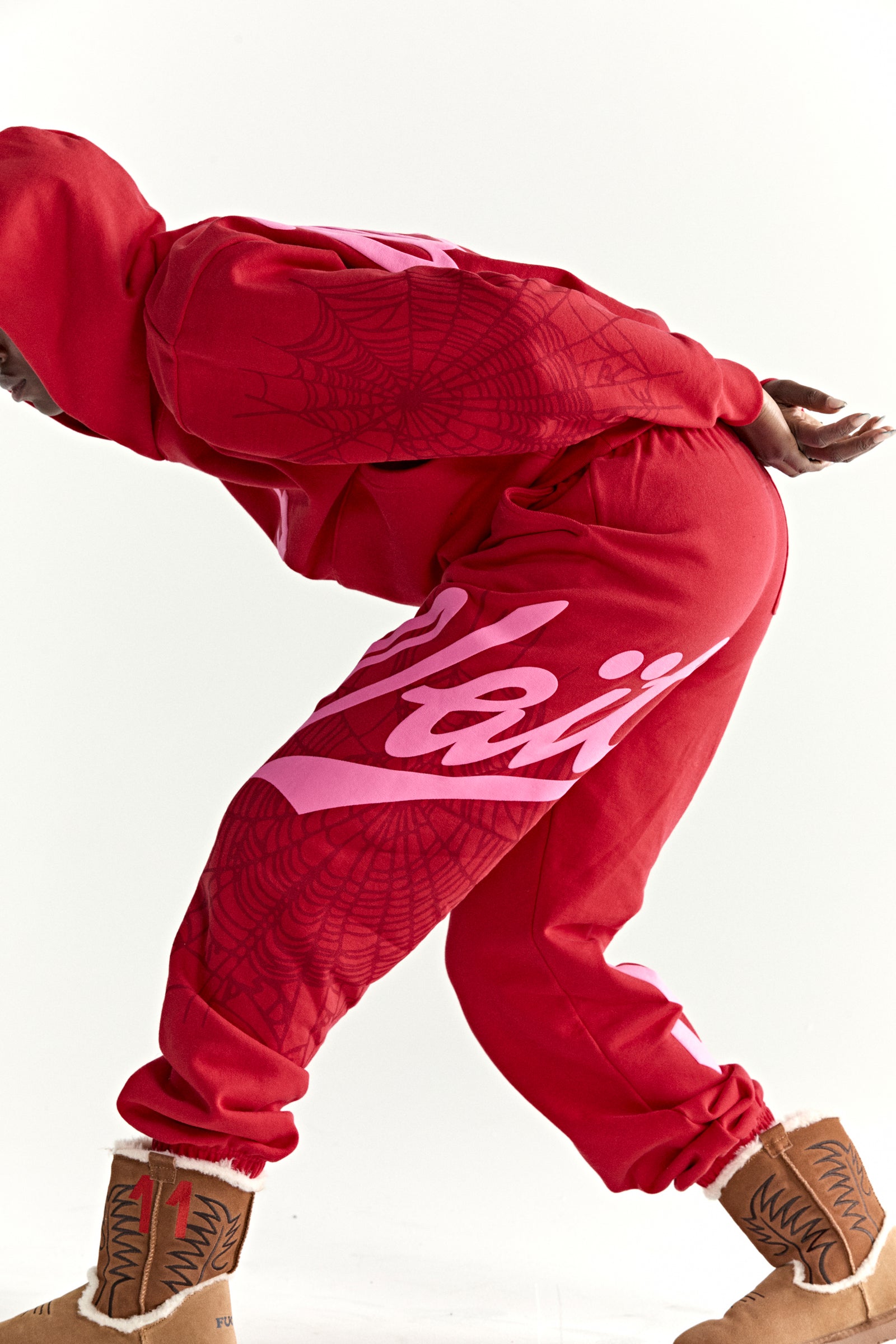 Red 13oz cotton fleece hoodie and sweatpants with pink puff print, spiderweb details, and script text.