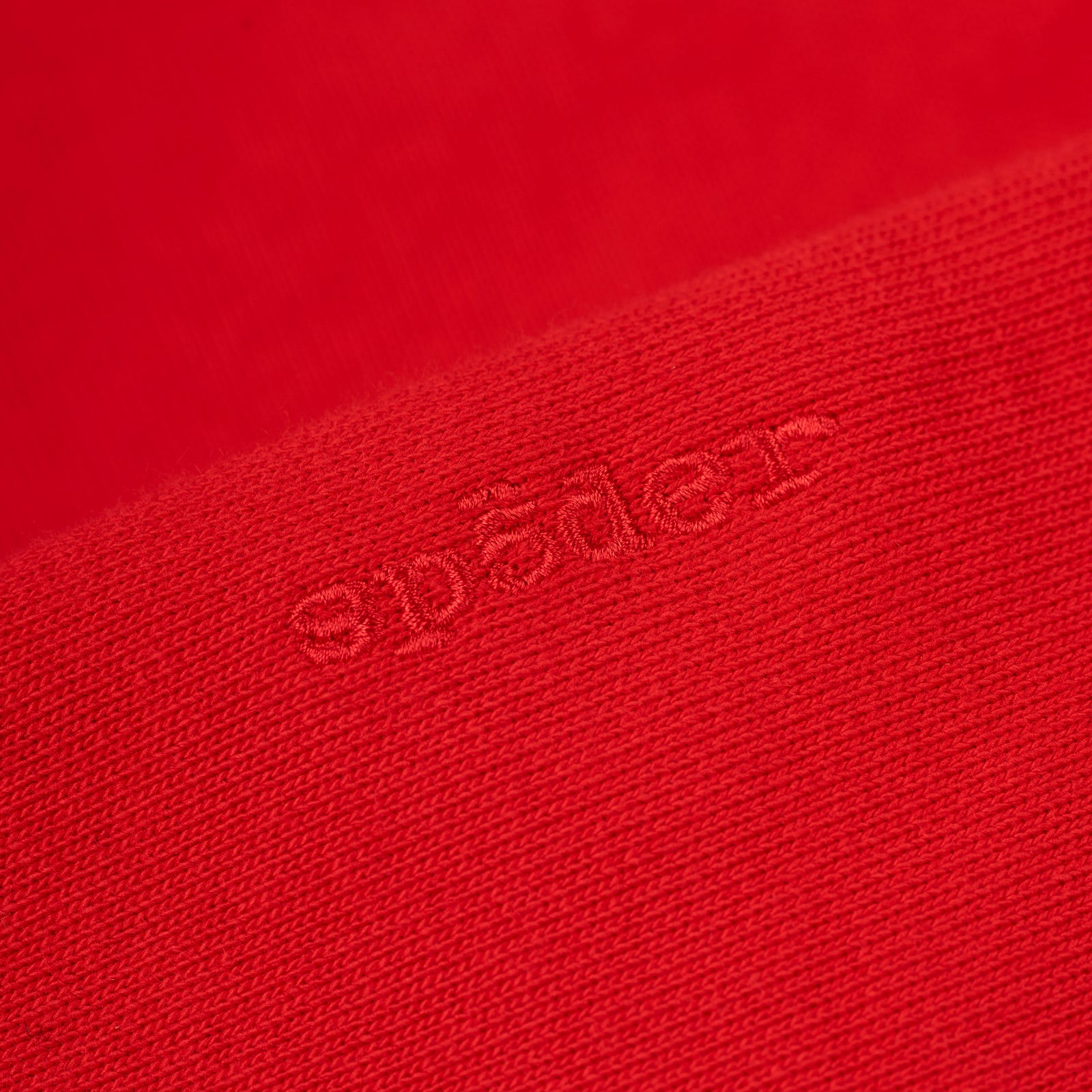 Close-up of a red 100% cotton fleece hoodie with embroidered "spades" text.