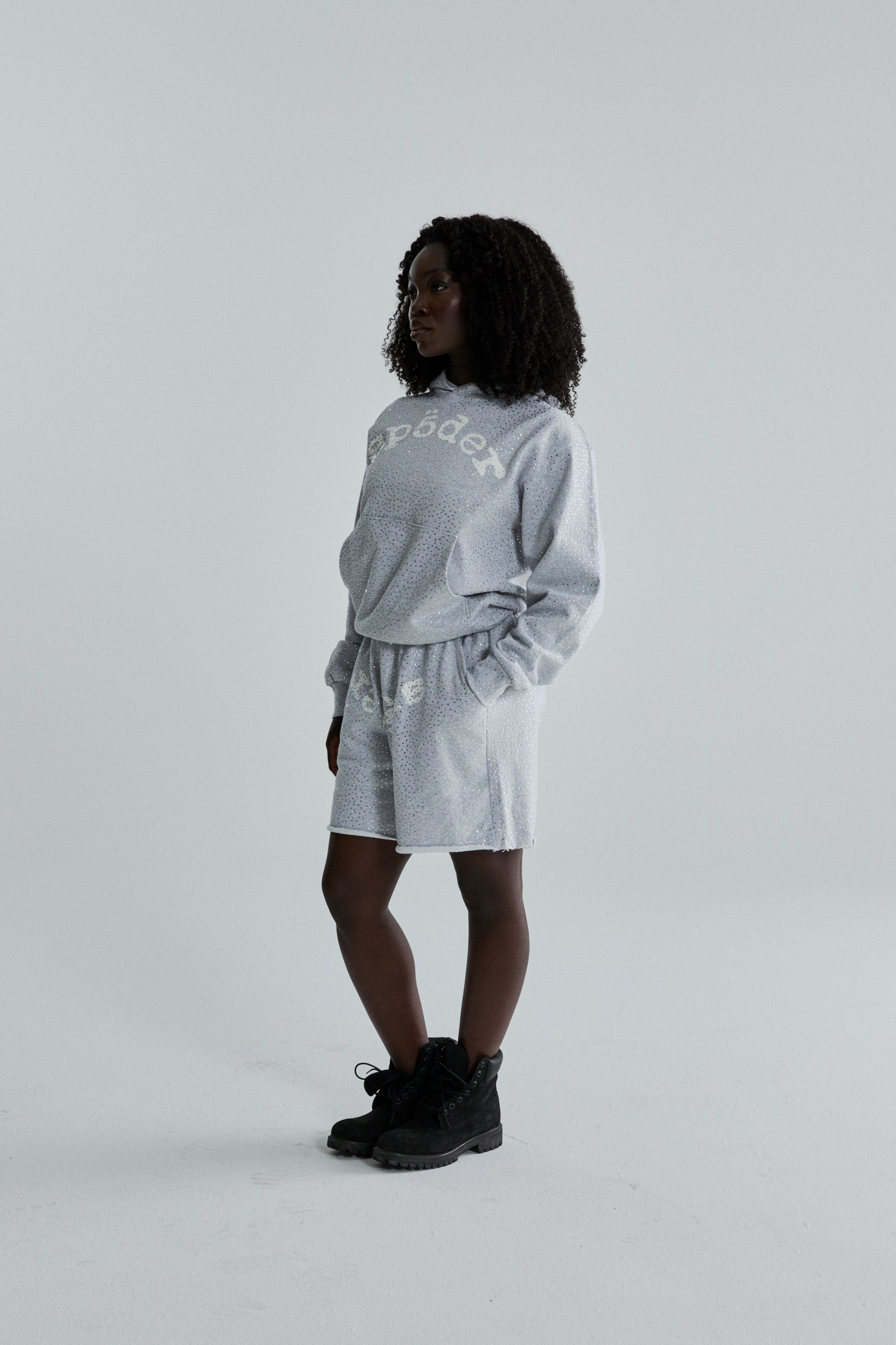 Woman in light gray VVS HOODIE and shorts with tonal rhinestones and SP5DER text.
