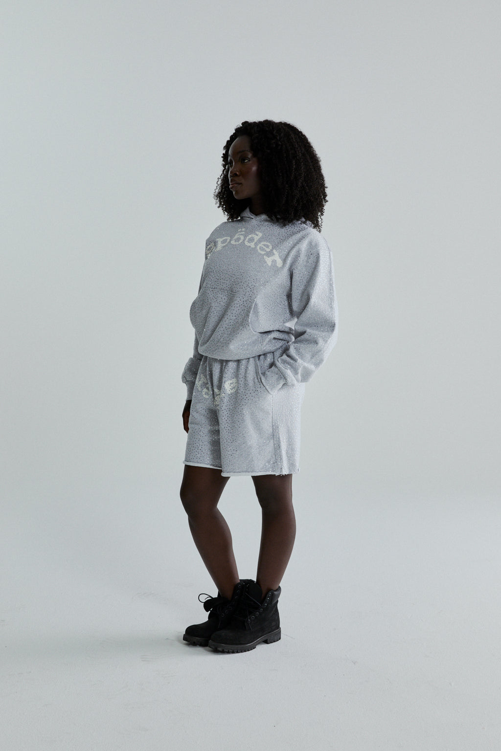 Woman in light gray VVS HOODIE and shorts with tonal rhinestones and SP5DER text.