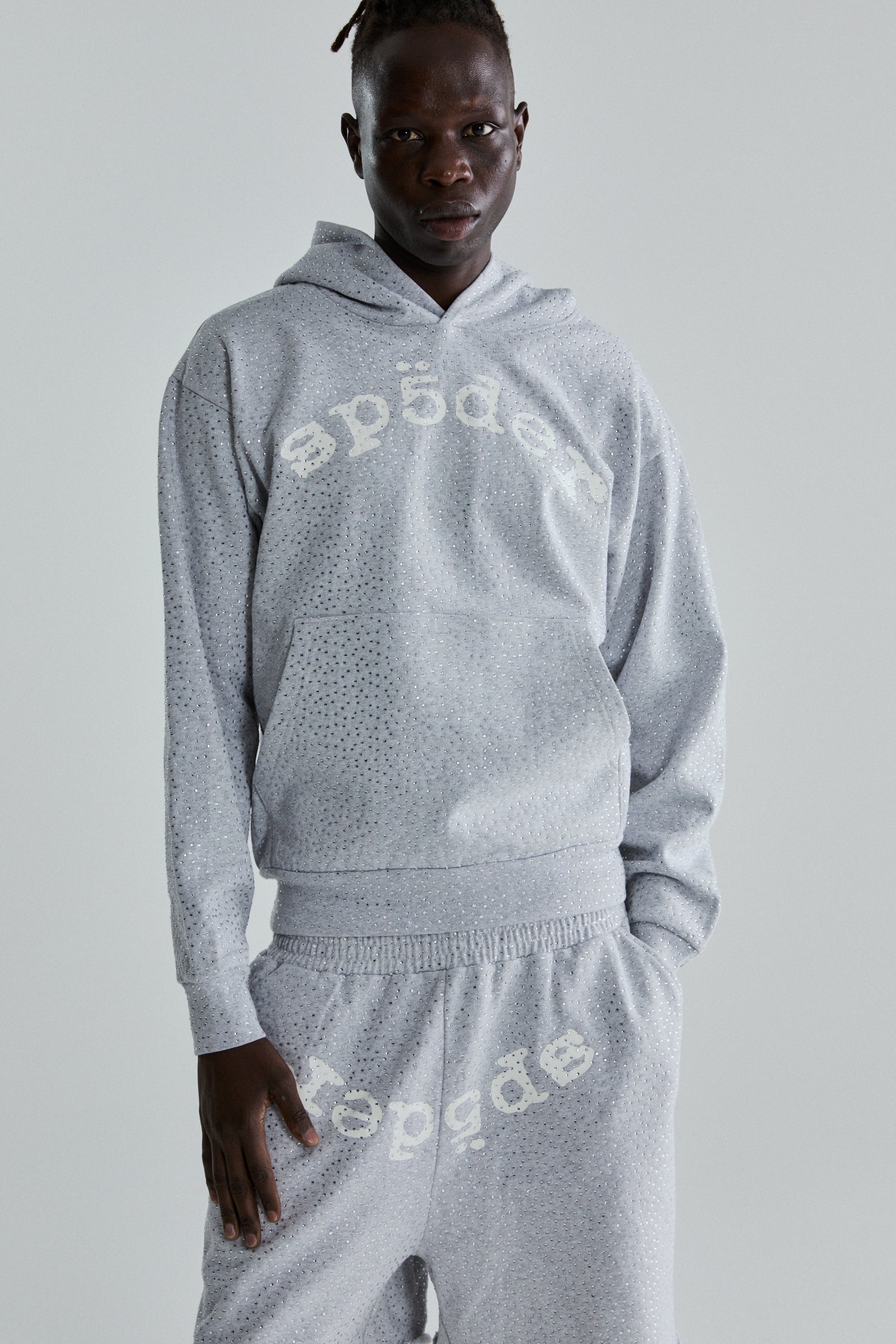 Model wearing a grey VVS Hoodie and sweatpants with all-over tonal rhinestones and "SP5DER" text.