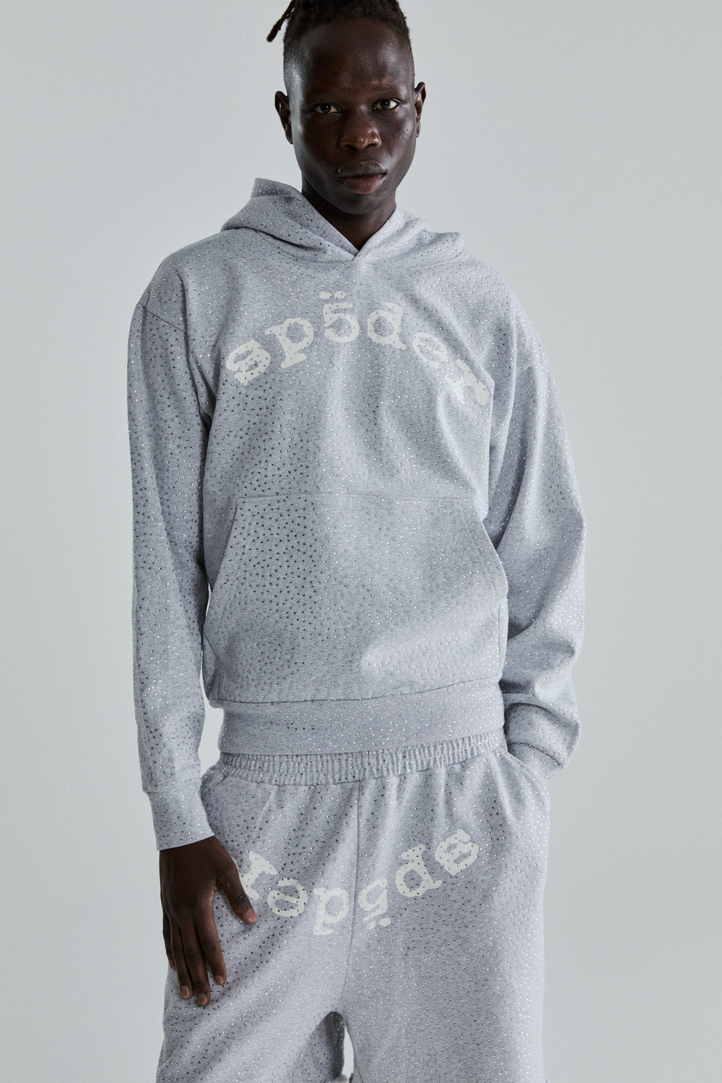 Model wearing a grey VVS Hoodie and sweatpants with all-over tonal rhinestones and "SP5DER" text.