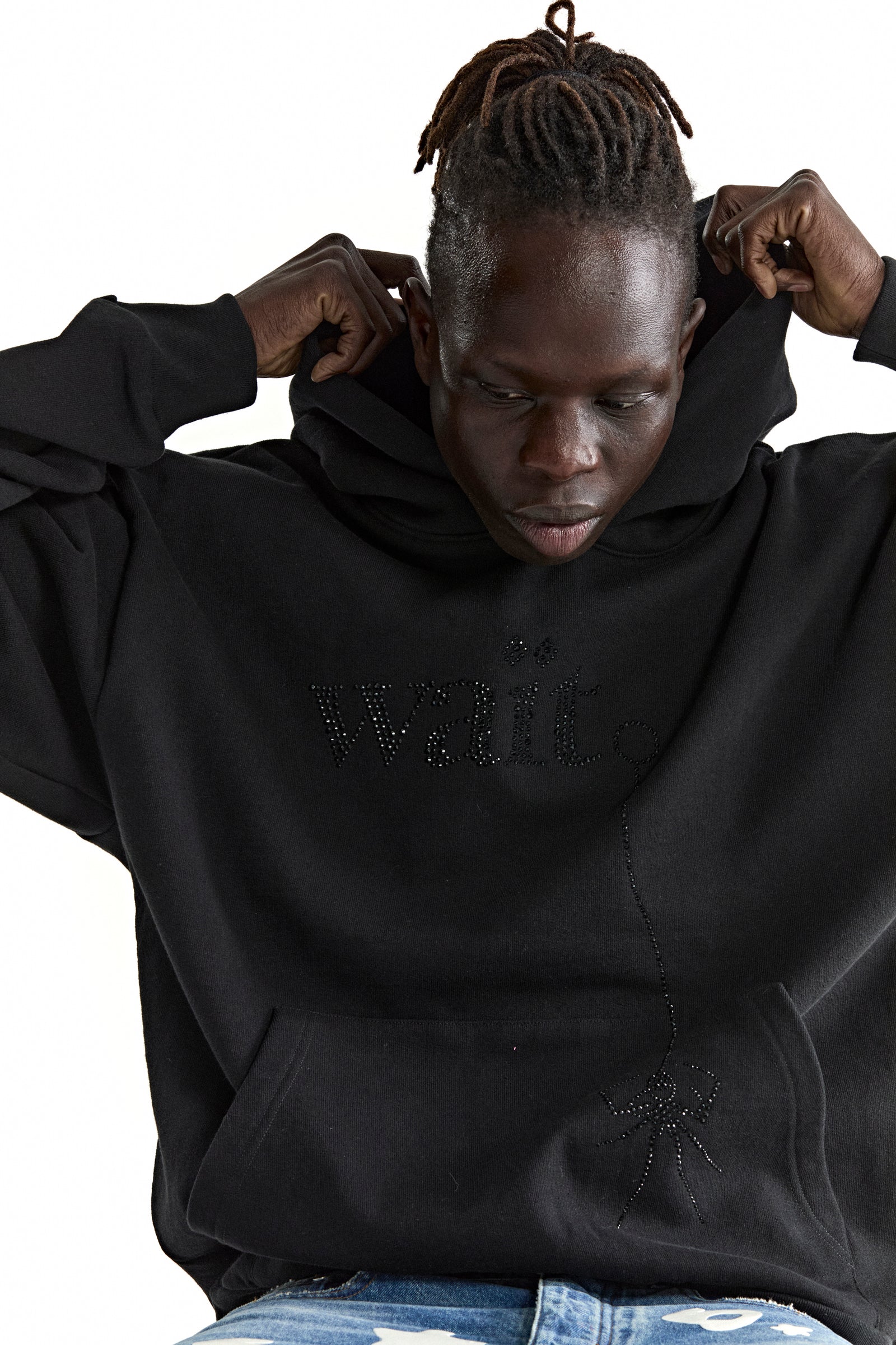 Black cotton fleece hoodie with rhinestone "Wait" detail and spider graphic, worn by a person adjusting the hood.
