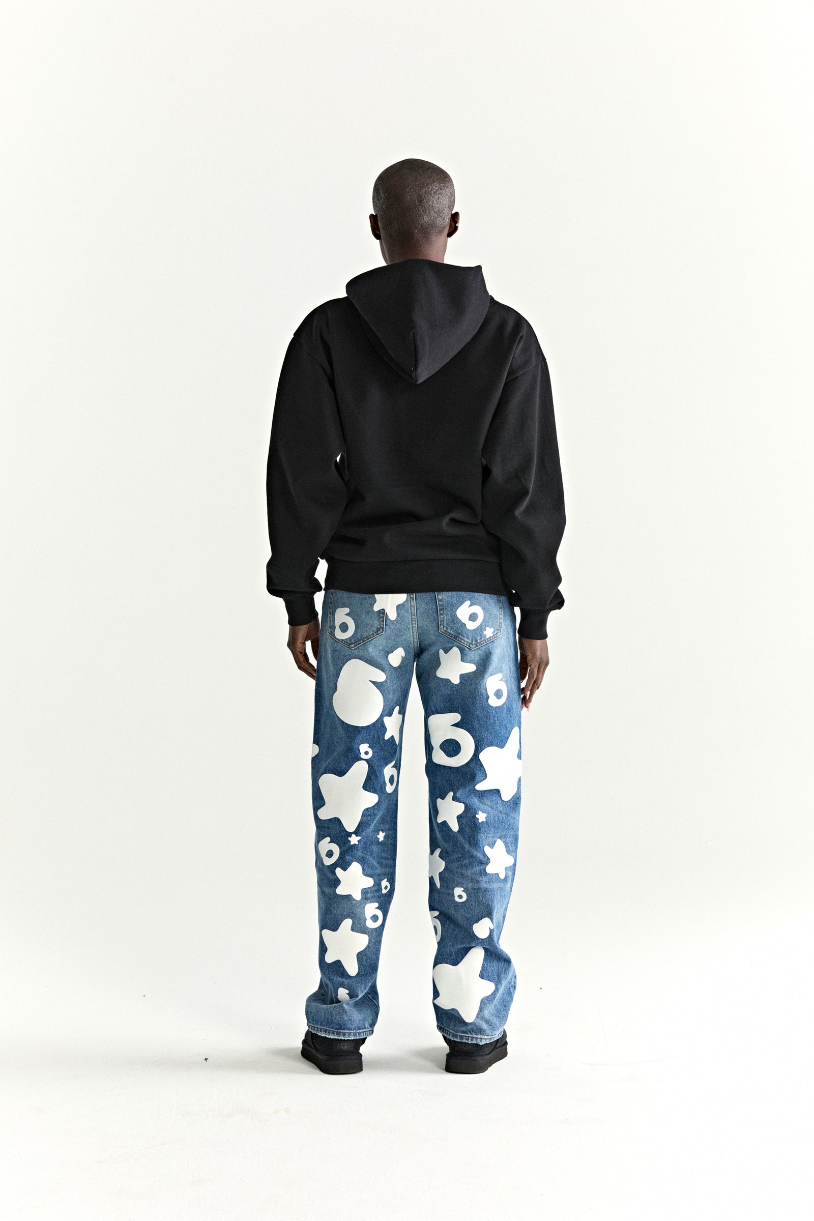 Person from behind wearing a black WAIT STONE HOODIE with a rhinestone 'Wait' detail, paired with blue jeans.